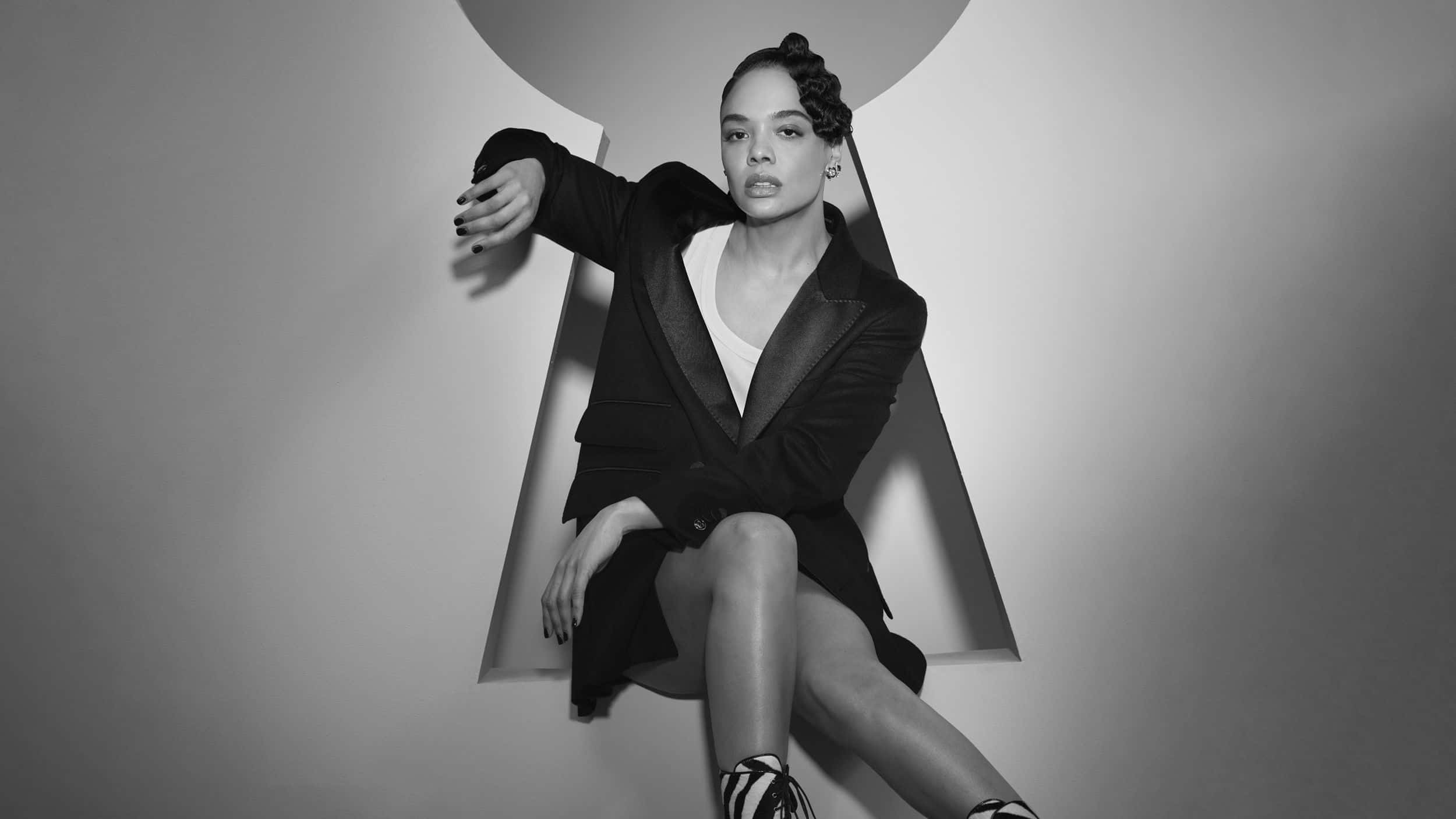 Black And White Fashion 桌布 壁紙 — 一位沉穩的女性穿著黑色西裝外套，自信地坐在幾何光線切割內，背景為極簡黑白風格。