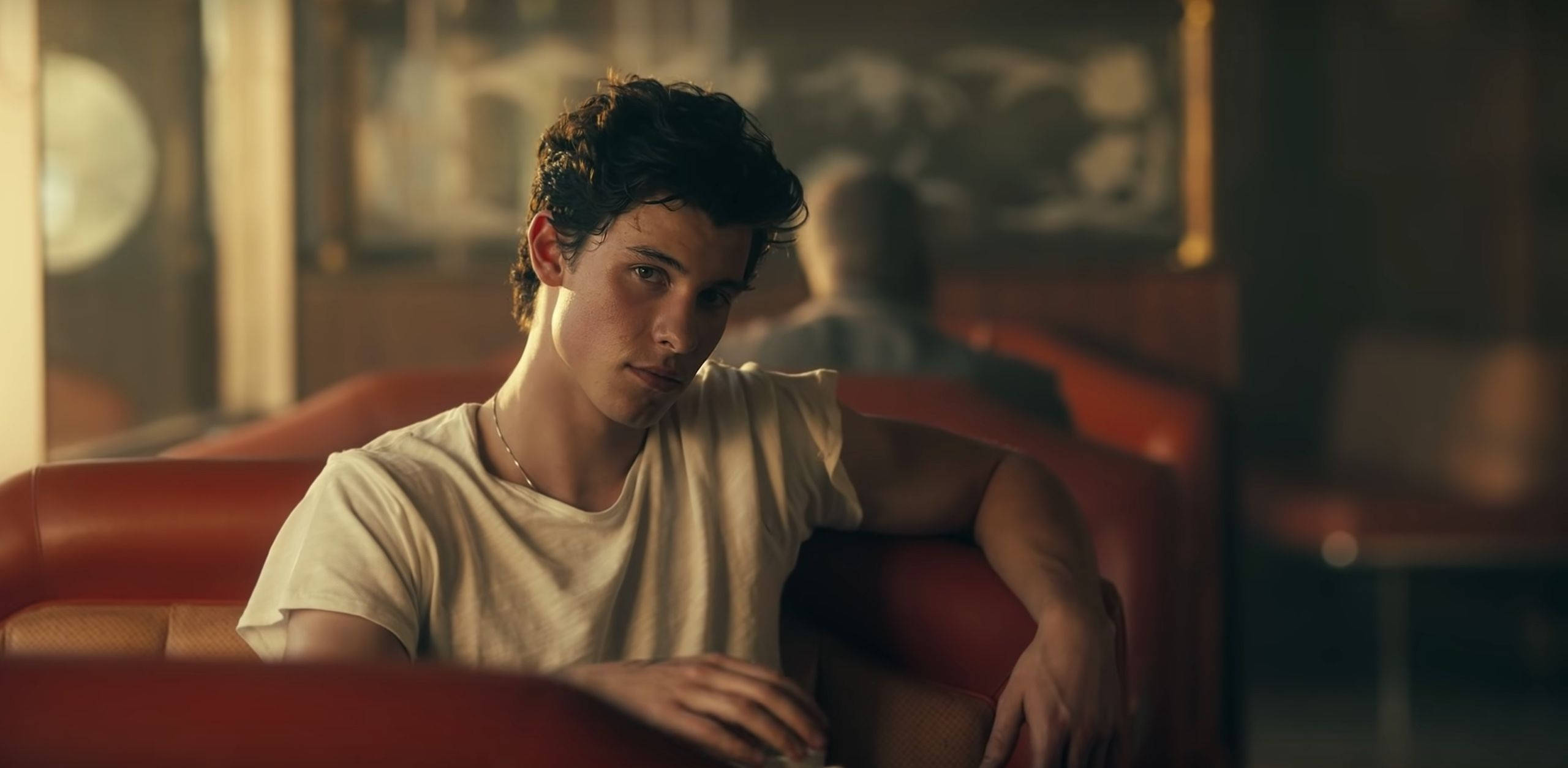 Shawn Mendes《Señorita》 壁紙 — 一位深色捲髮的年輕男子坐在溫暖燈光的復古餐廳紅色皮革卡座上，若有所思。