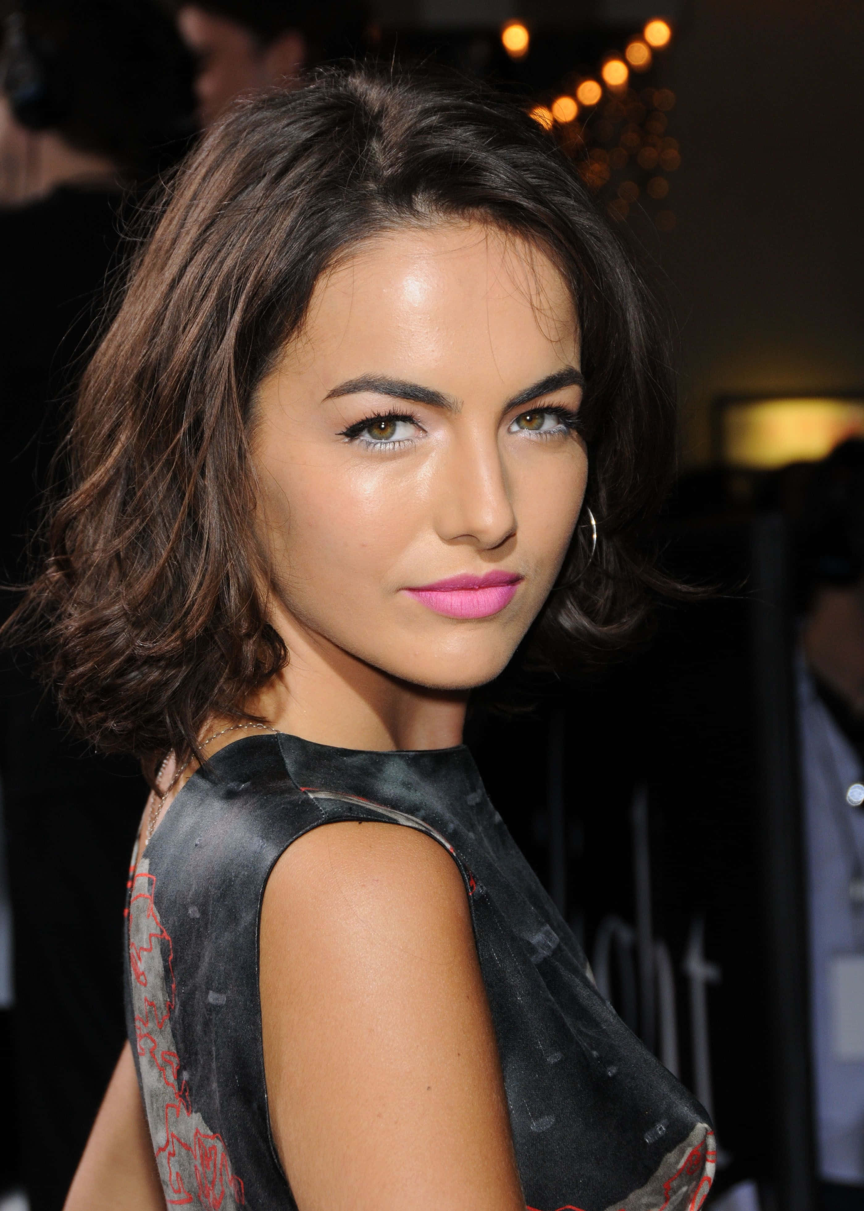Camilla Belle 桌布 壁紙 — 一位深色波浪長髮、塗著大膽粉紅色唇膏的女性，回頭望向鏡頭的近距離肖像。