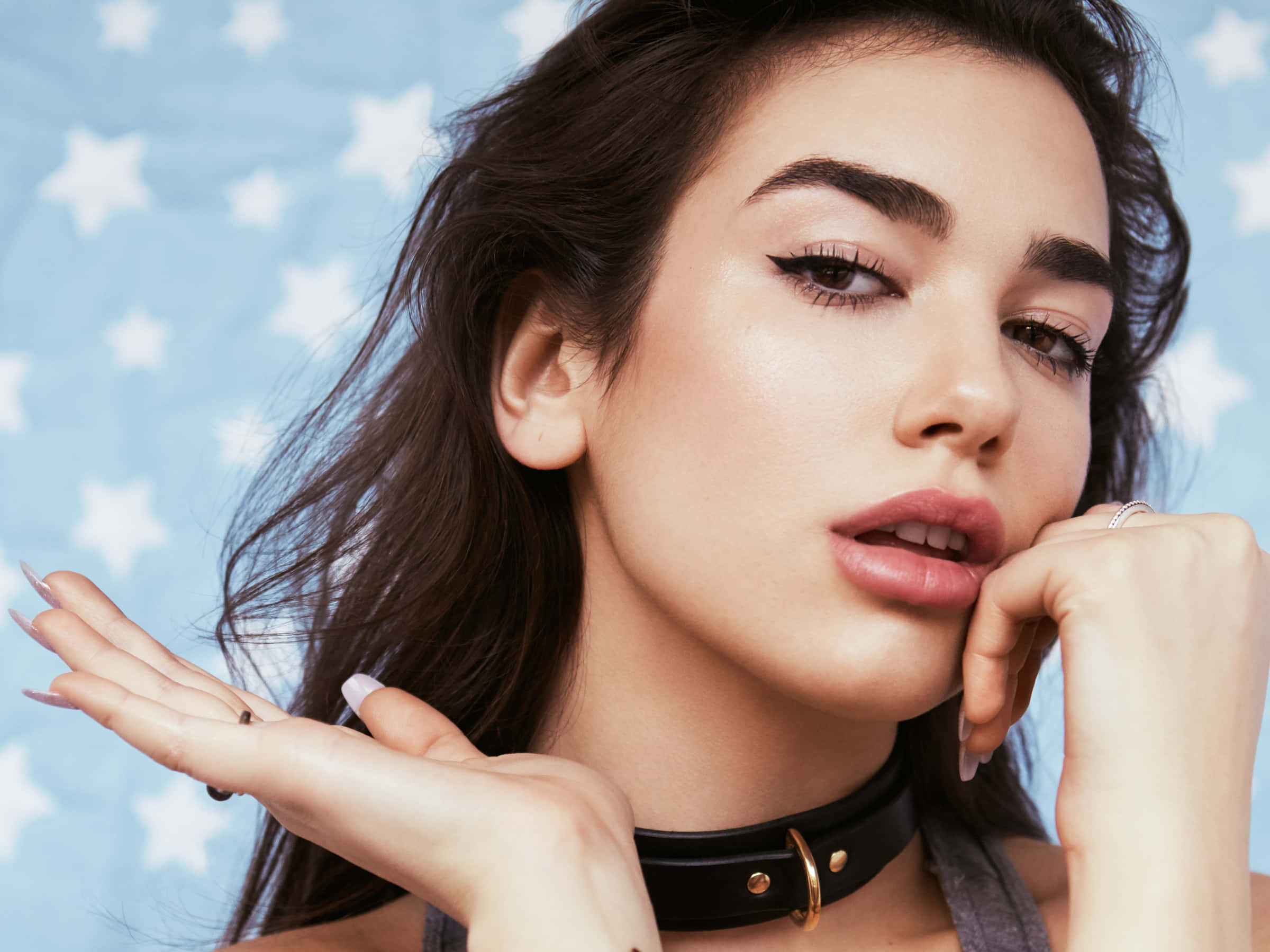 Dua Lipa 桌布 壁紙 — 一位深色頭髮、妝容大膽的女性，在藍色星星圖案背景前戴著黑色頸鍊擺姿勢。