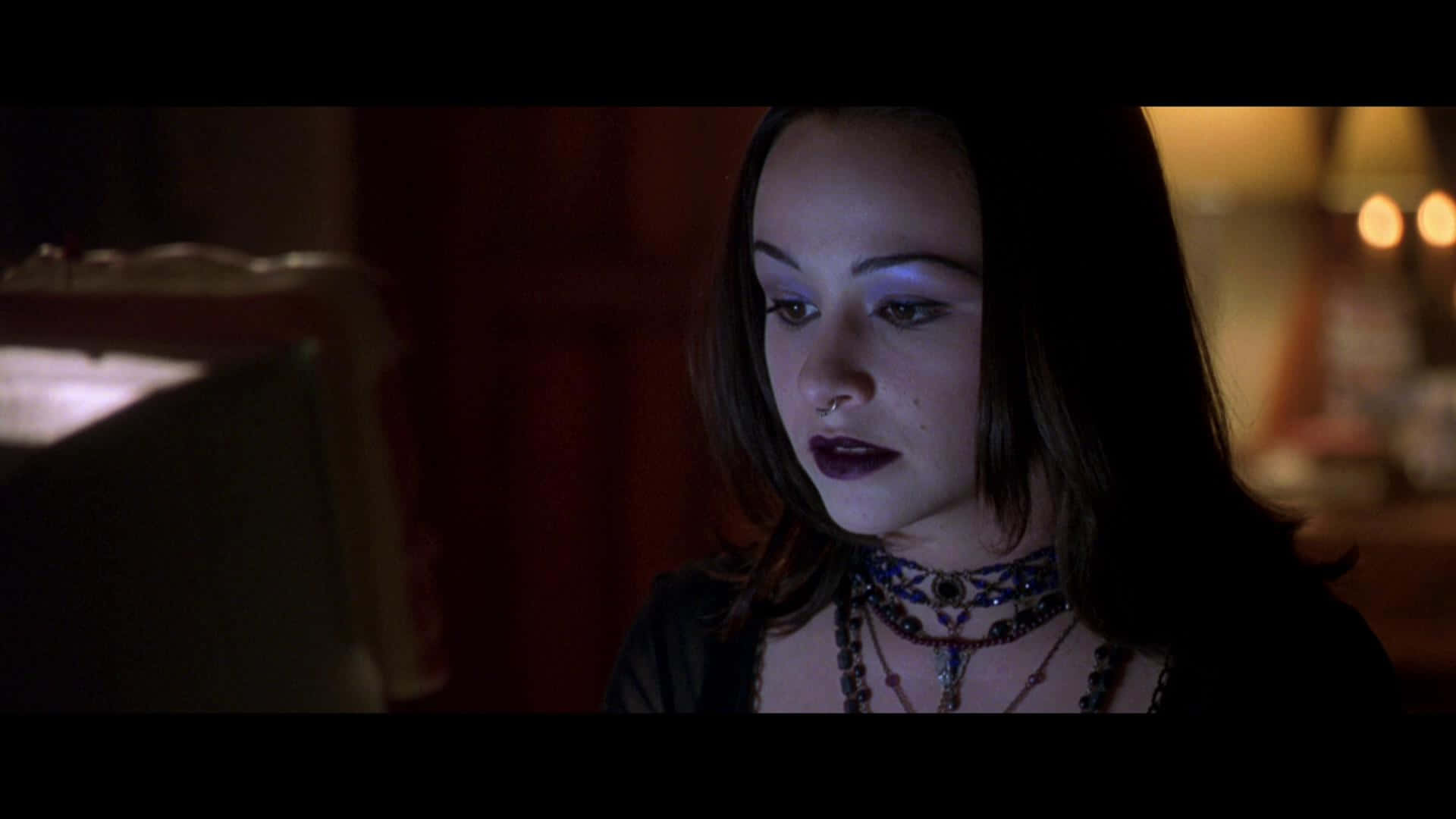 Danielle Harris 桌布 壁紙 — 一位深色頭髮、妝容大膽的年輕女性在昏暗的房間裡，在溫暖的環境燈光下低頭凝視。