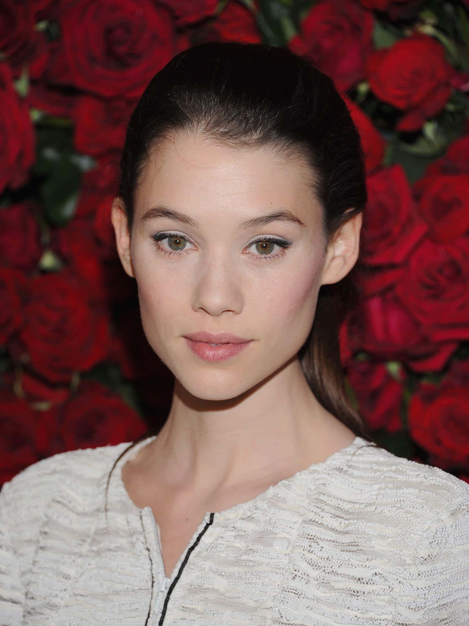 Astrid Berges Frisbey 桌布 壁紙 — 一位深色頭髮、妝容柔和、姿態優雅嘅女性，喺茂盛鮮豔嘅紅玫瑰背景下向前凝視。