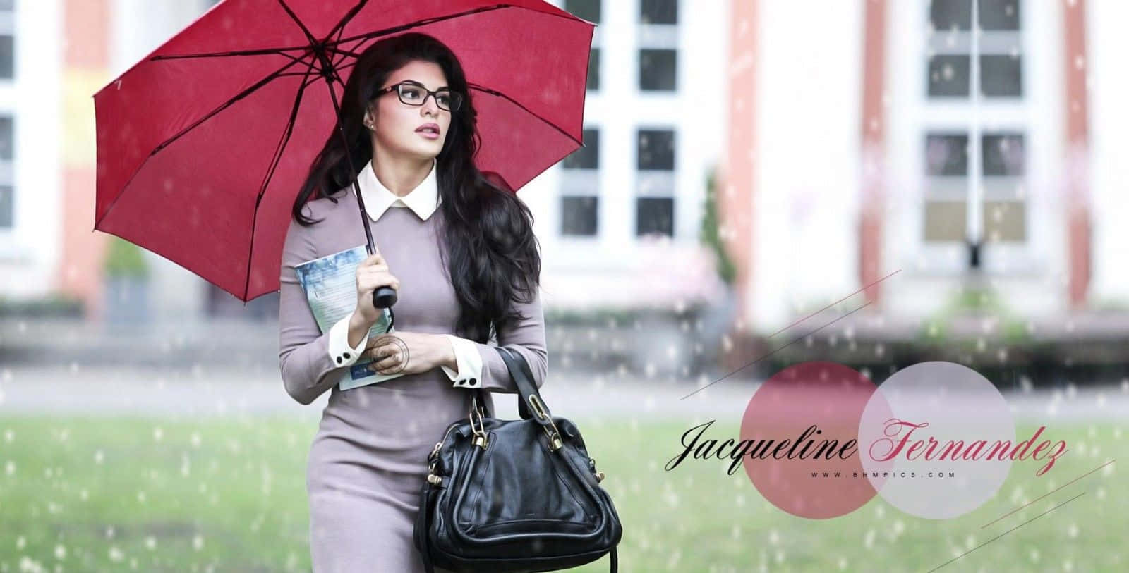 Jacqueline Fernandez 桌布 壁紙 — 一位深色頭髮、戴眼鏡的女性，在大雨中撐著紅色雨傘，在建築物附近行走。