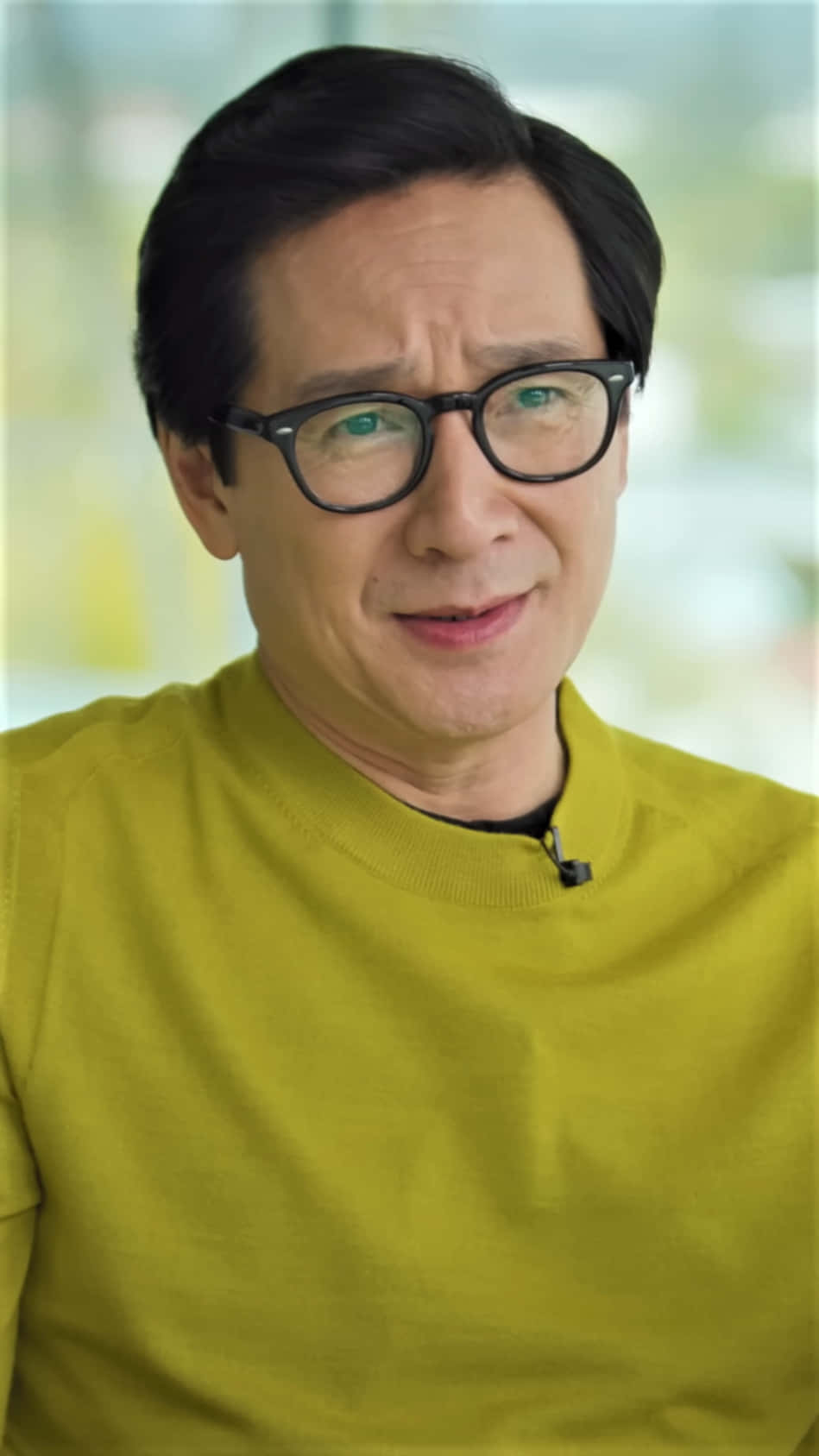 Ke Huy Quan 桌布 壁紙 — 一位深色頭髮、戴眼鏡的男士穿著亮黃色襯衫，微微向右看，帶著溫柔的微笑。