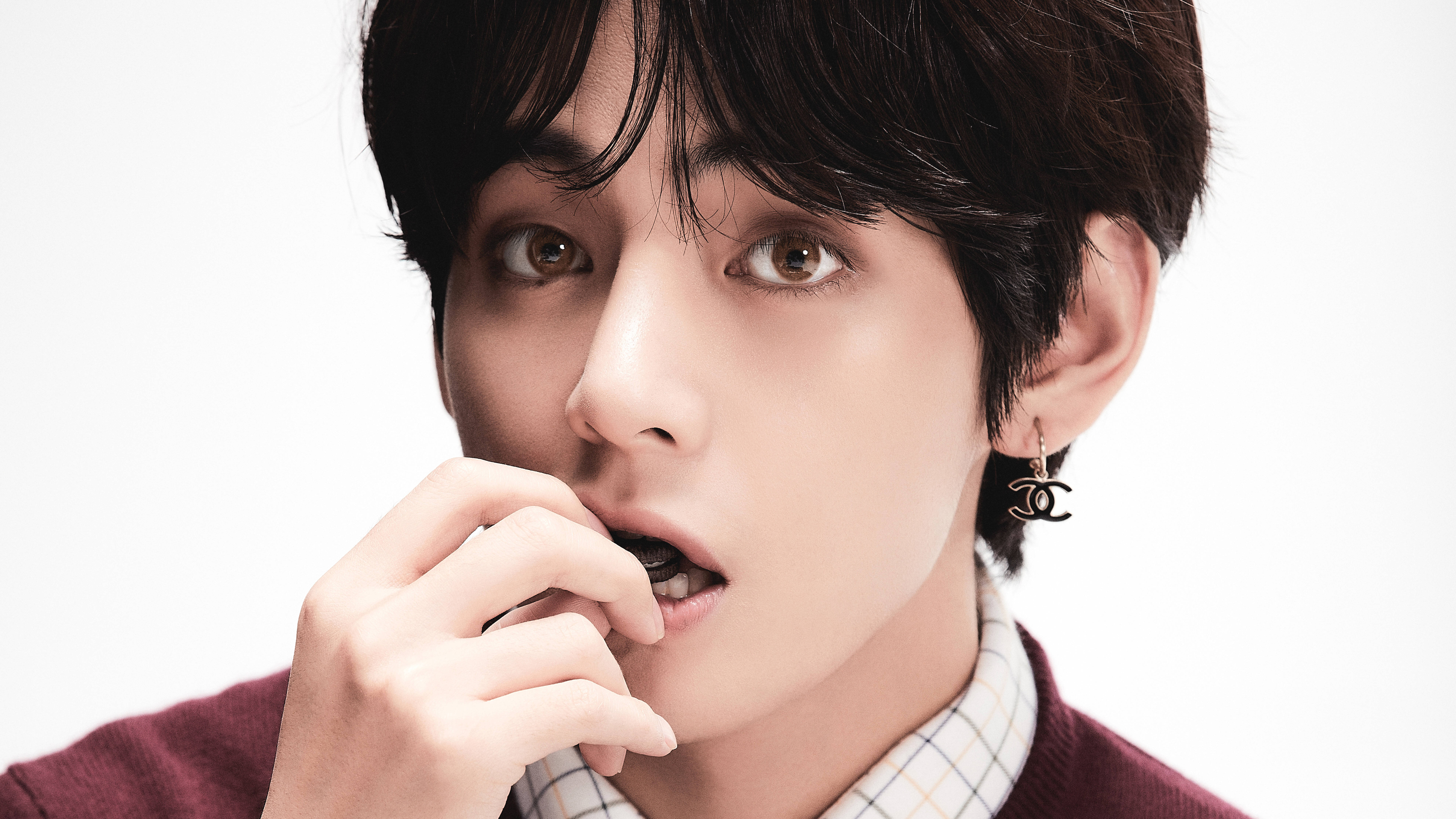 BTS Taehyung MOTS 7 壁紙 — 一位深色頭髮、戴著 Chanel 耳環的年輕男子，在白色背景前咬著手指，專注地看著鏡頭。