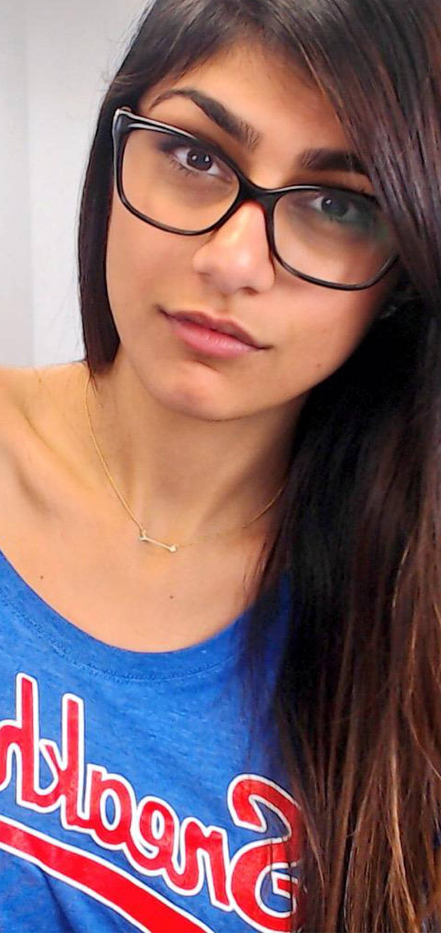 sexy babe 桌布 壁紙 — 一位深色頭髮、戴黑色粗框眼鏡的年輕女性，穿著藍色棒球風格襯衫，直視鏡頭。