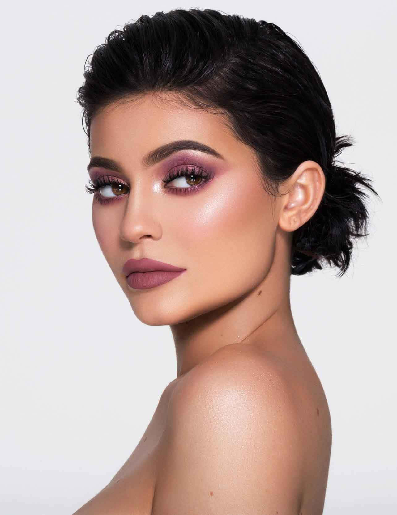 Kylie Jenner 桌布 壁紙 — 一位深色頭髮、梳著光滑髮髻、塗著大膽紫色眼影的女性，在純白背景前回頭凝視。