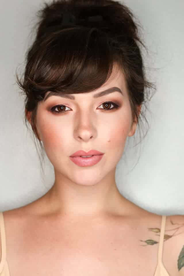 Spring Makeup 桌布 壁紙 — 一位深色頭髮、梳著凌亂髮髻、化著柔和妝容的女性，在純淺灰色背景前直視鏡頭。