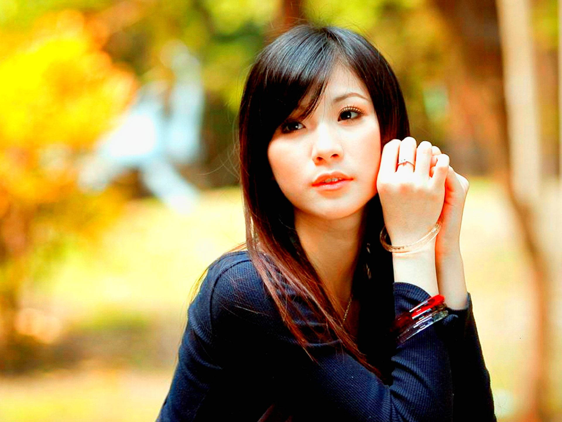 Beautiful Woman 桌布 壁紙 — 一位深色頭髮、神情深思的年輕女子，在溫暖的秋季模糊背景下，用手托著下巴。