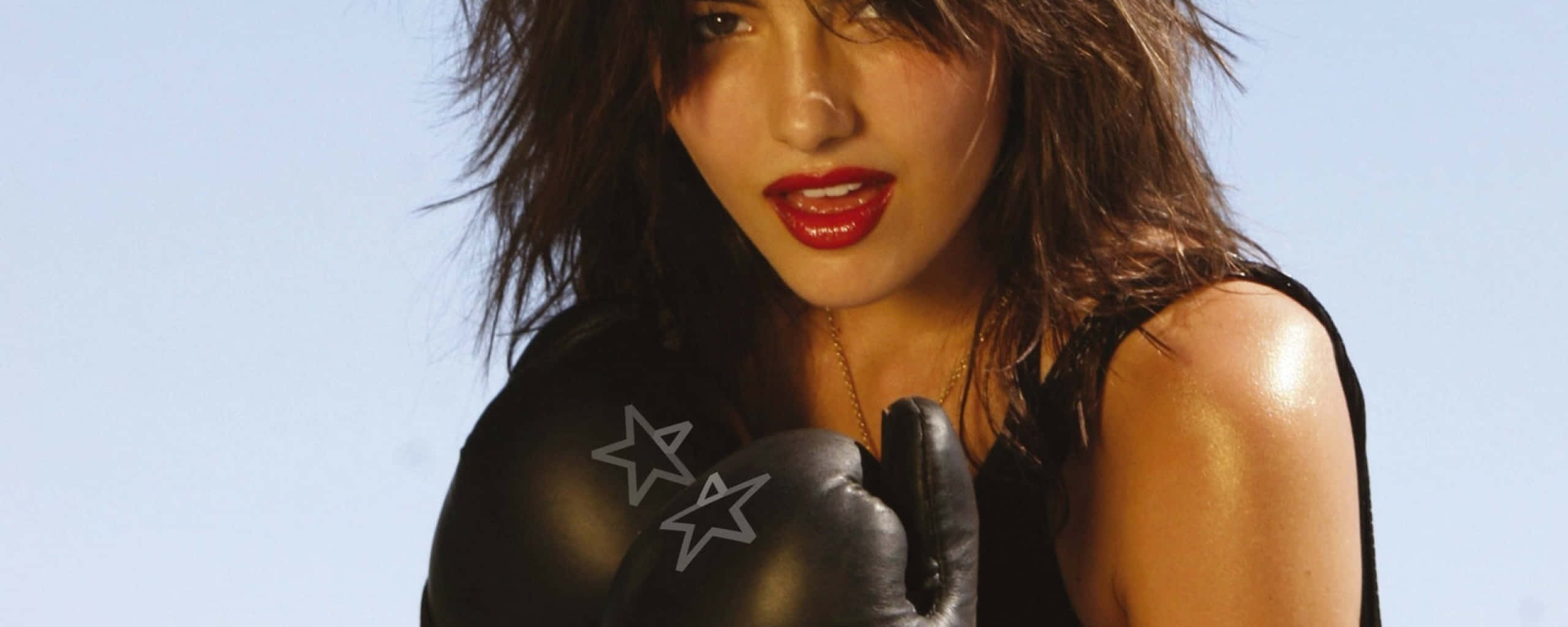 Camilla Belle 桌布 壁紙 — 一位深色頭髮、紅唇的女性，在淡藍色天空下戴著黑色拳擊手套。