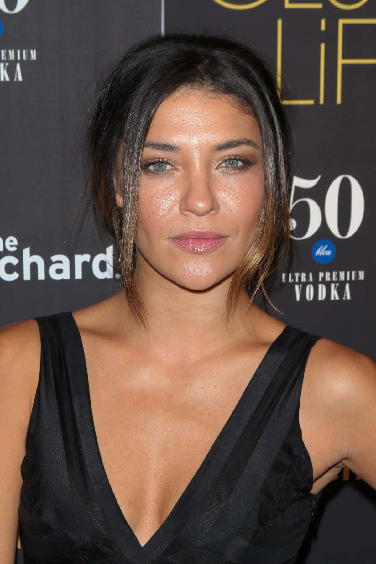 jessica szohr 桌布 壁紙 — 一位深色頭髮、綠色眼睛的女性，在一個帶有品牌背景的華麗活動中穿著黑色連衣裙。