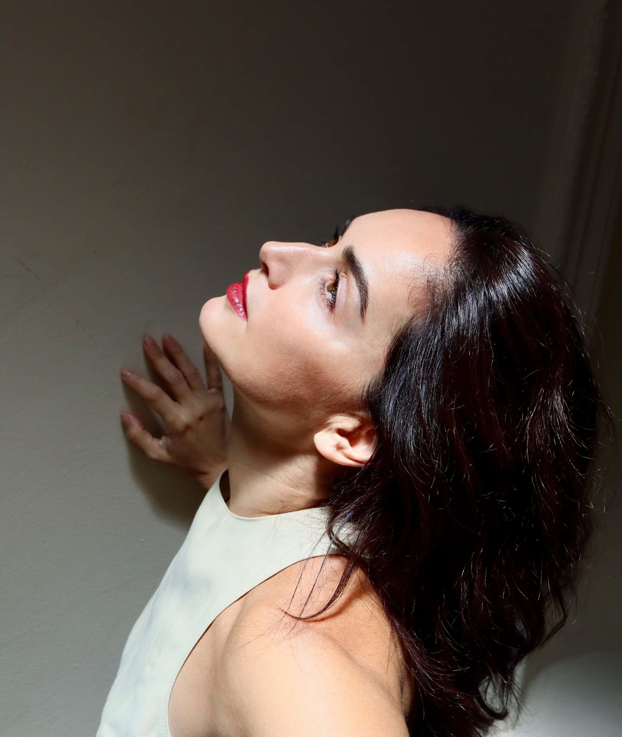 Ana De La Reguera 桌布 壁紙 — 一位深色頭髮和紅唇的女性，面向素牆向上凝視，手輕輕放在牆面上。