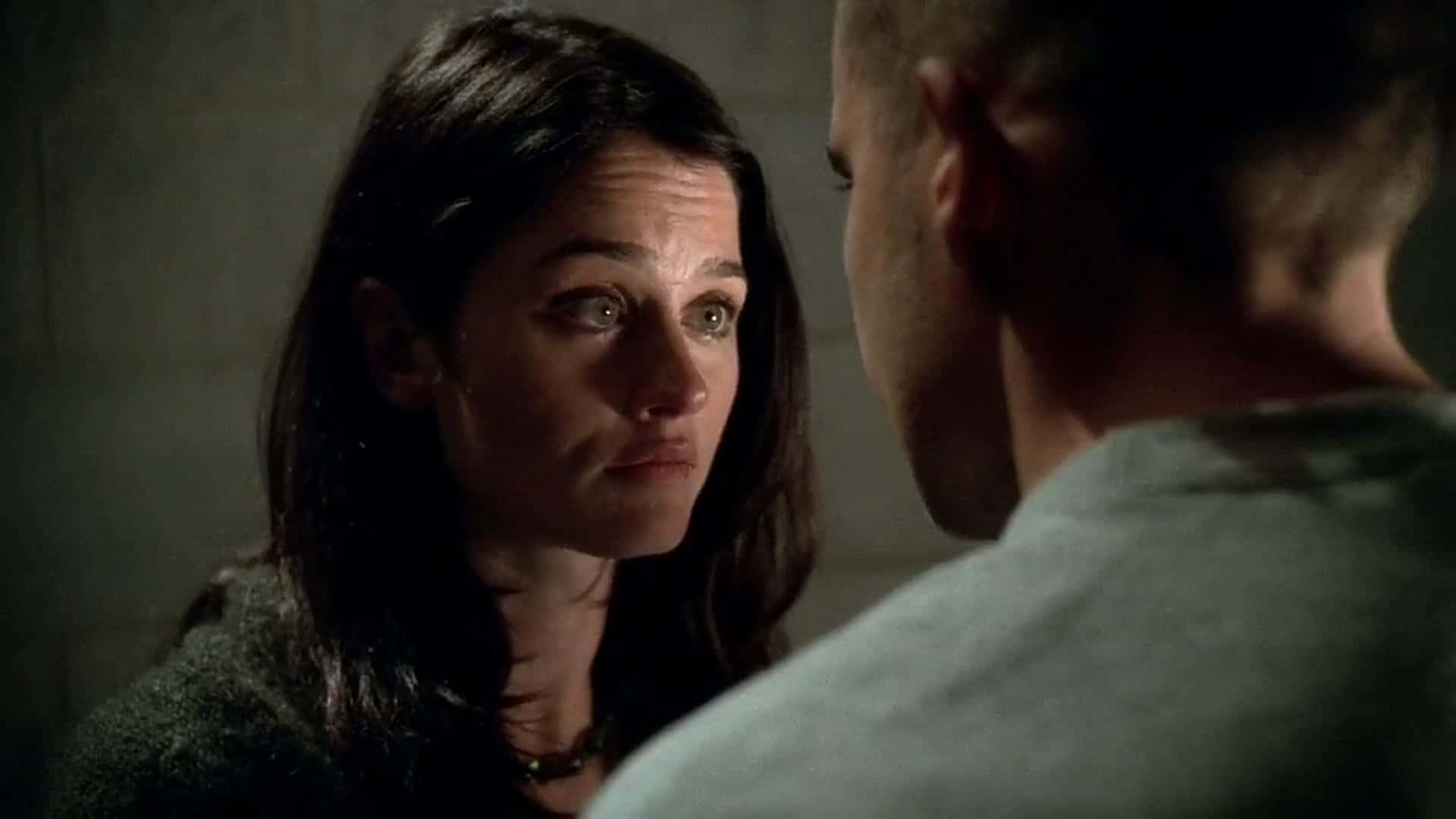 Robin Tunney 桌布 壁紙 — 一位深色頭髮的女人在一個光線昏暗、牆壁有紋理的房間裡專注地凝視著一個男人。