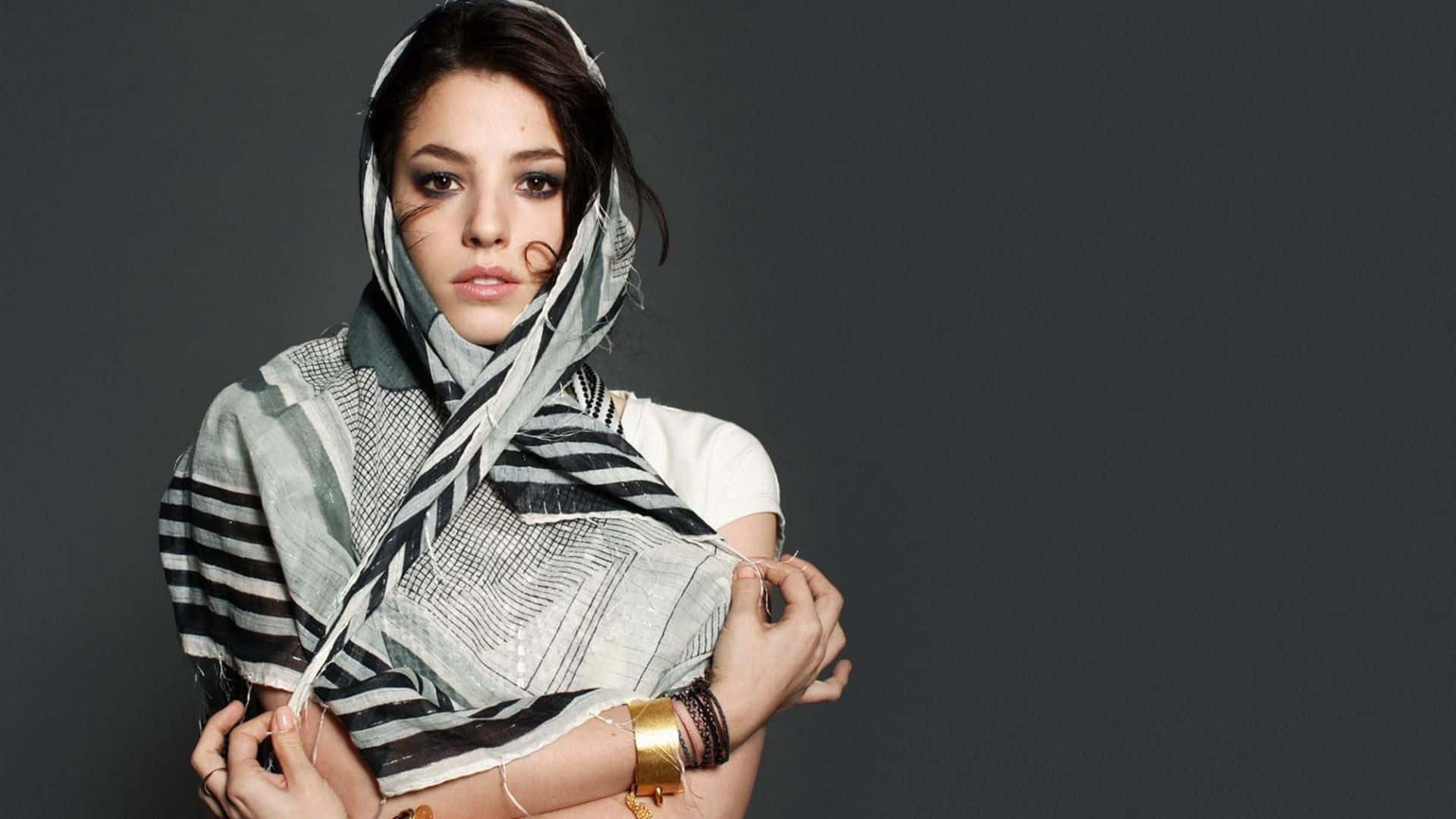 Olivia Thirlby 桌布 壁紙 — 一位深色頭髮的女性，在純灰色背景上，將一條圖案圍巾披在頭上和手臂上。