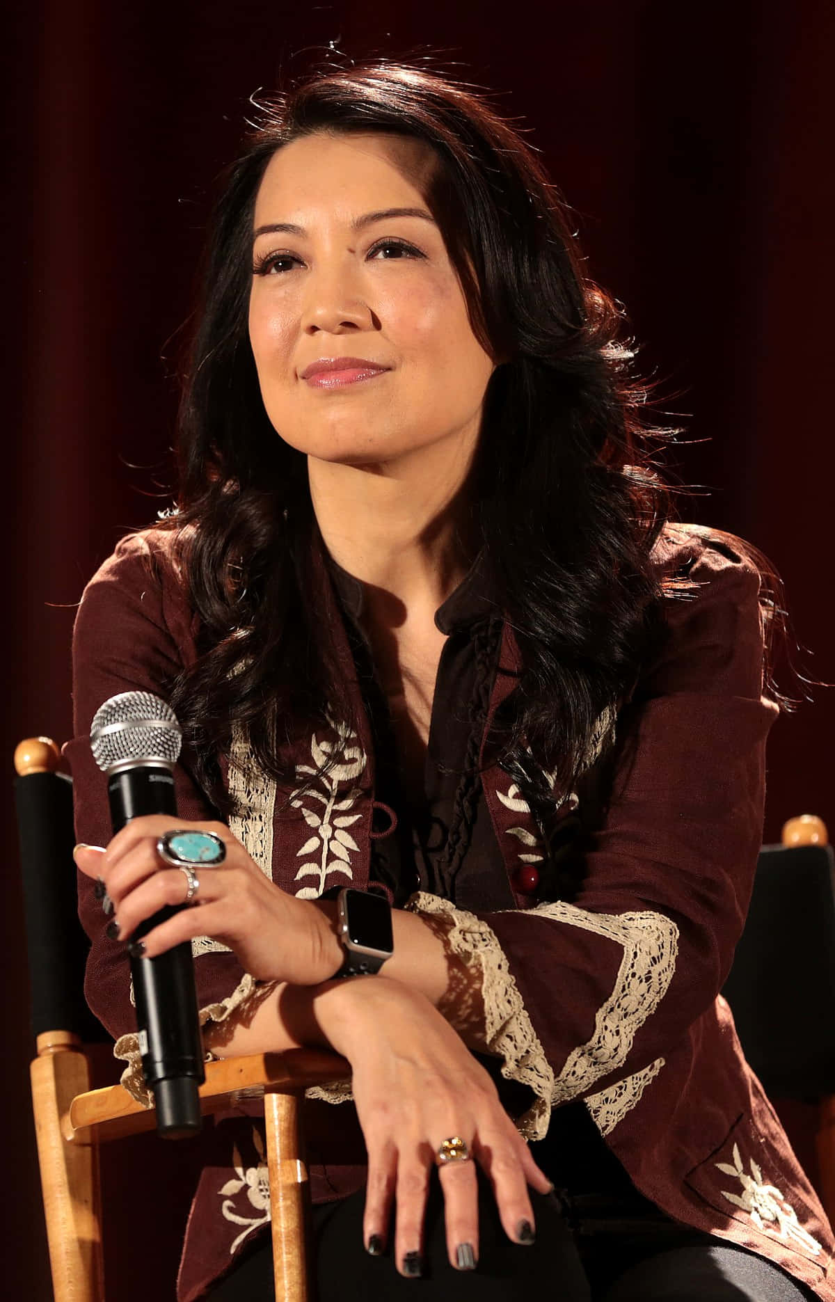 Ming Na Wen 桌布 壁紙 — 一位深色頭髮的女性坐在椅子上，手持麥克風，穿著帶有蕾絲細節的圖案棕色襯衫。