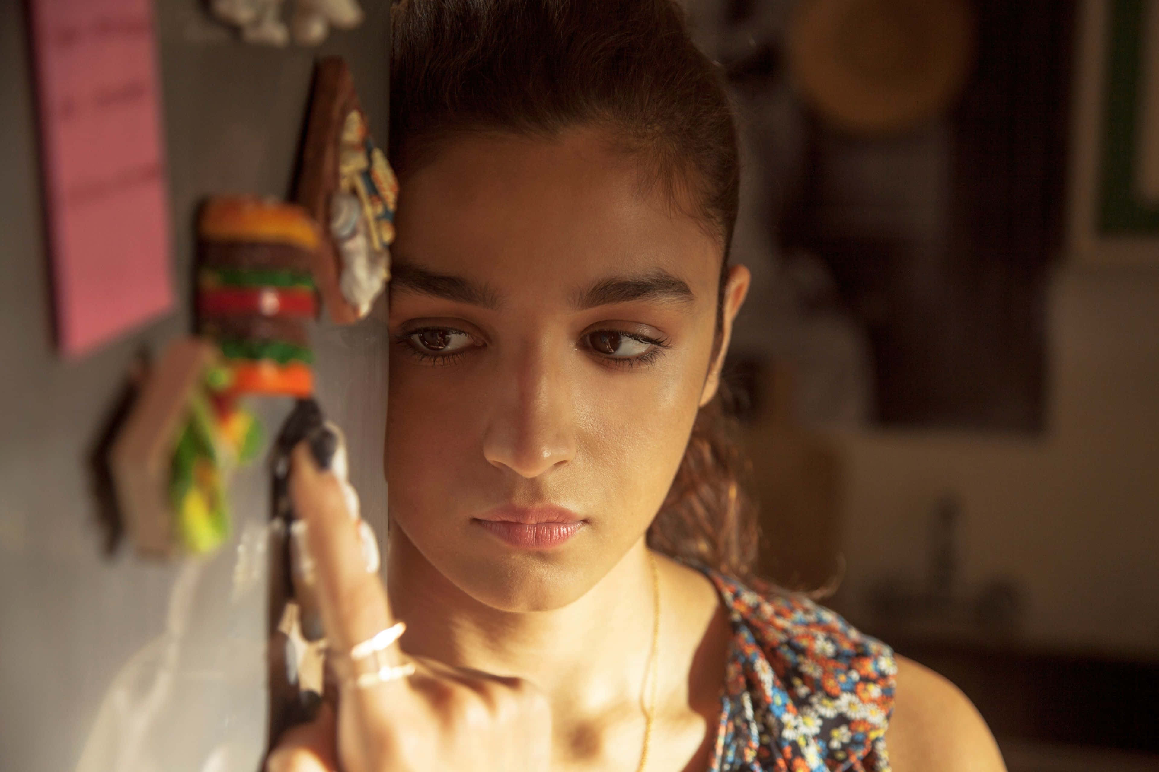 Alia Bhatt 桌布 壁紙 — 一位深色頭髮的年輕女子在溫暖照明的廚房裡，若有所思地將手指放在雪櫃門上。