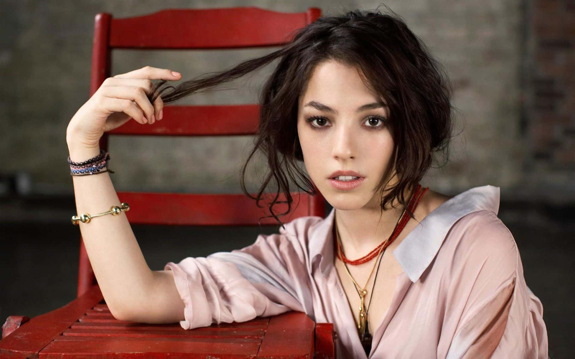Olivia Thirlby 桌布 壁紙 — 一位深色頭髮的年輕女性坐在紅色木椅上，輕輕觸摸頭髮，直視鏡頭。