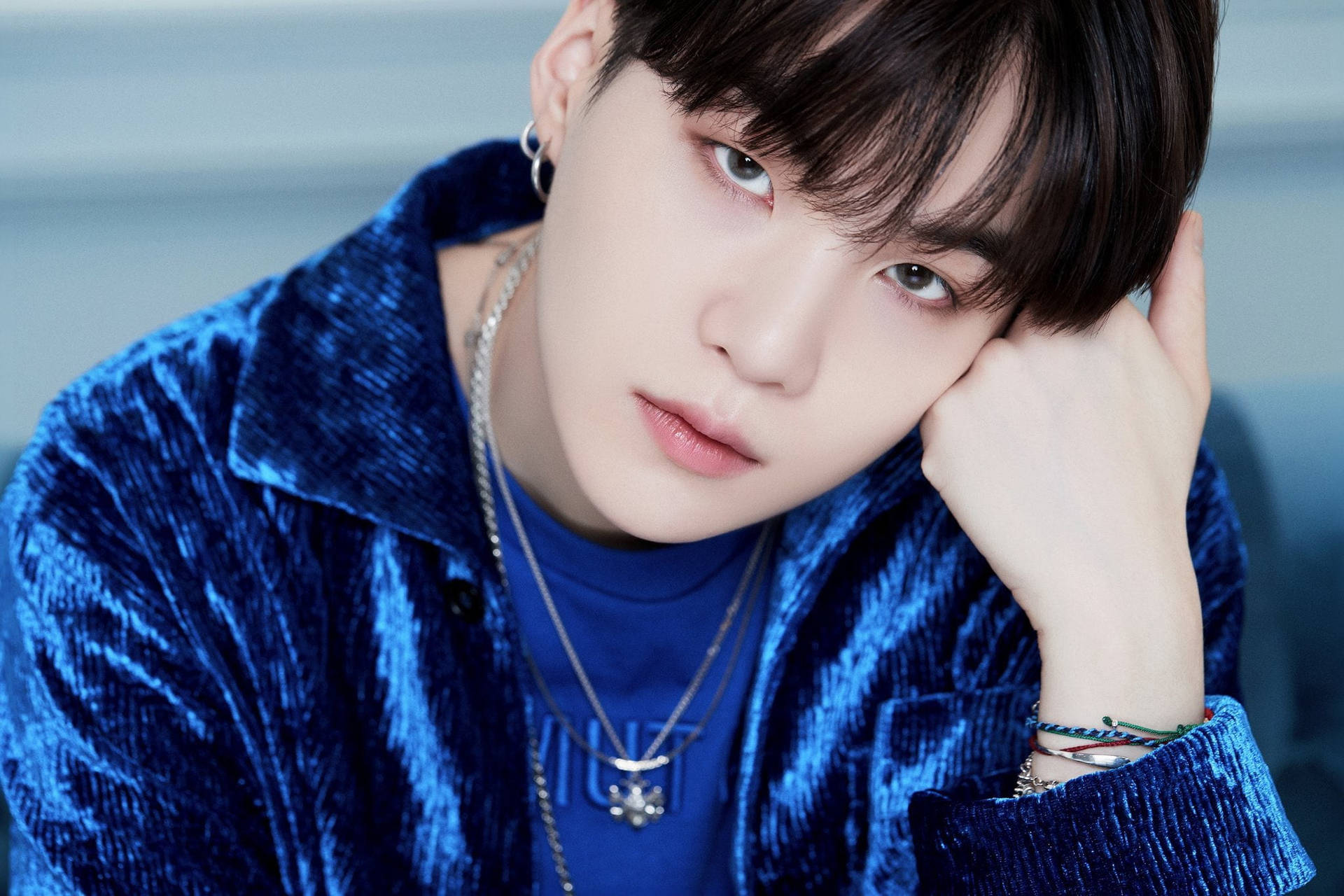 Suga BTS《Life Goes On》 壁紙 — 一位深色頭髮的年輕男子將頭靠在手上，身穿質感藍色天鵝絨外套和層疊項鍊。