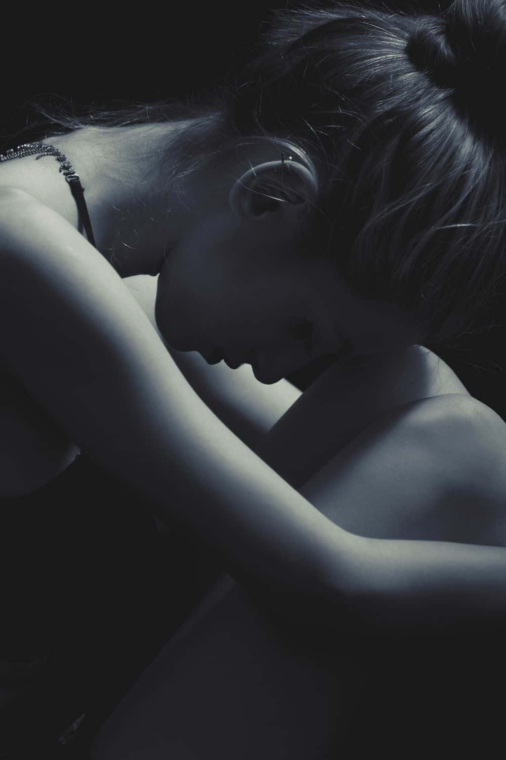 Dark Emo 桌布 壁紙 — 一位深色頭髮盤成髮髻的女性，在昏暗、憂鬱的藍調肖像中將頭靠在手臂上。