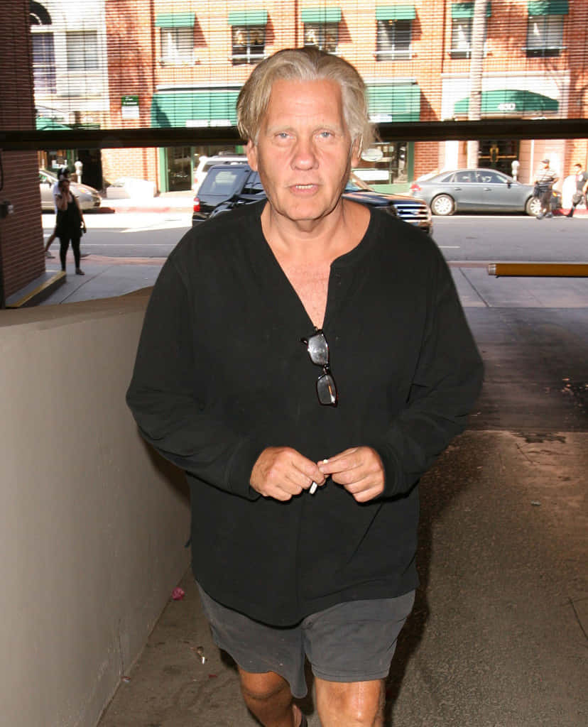 William Forsythe 桌布 壁紙 — 一位灰髮男子穿著黑色襯衫，太陽眼鏡掛在領口，走在城市行人路上。