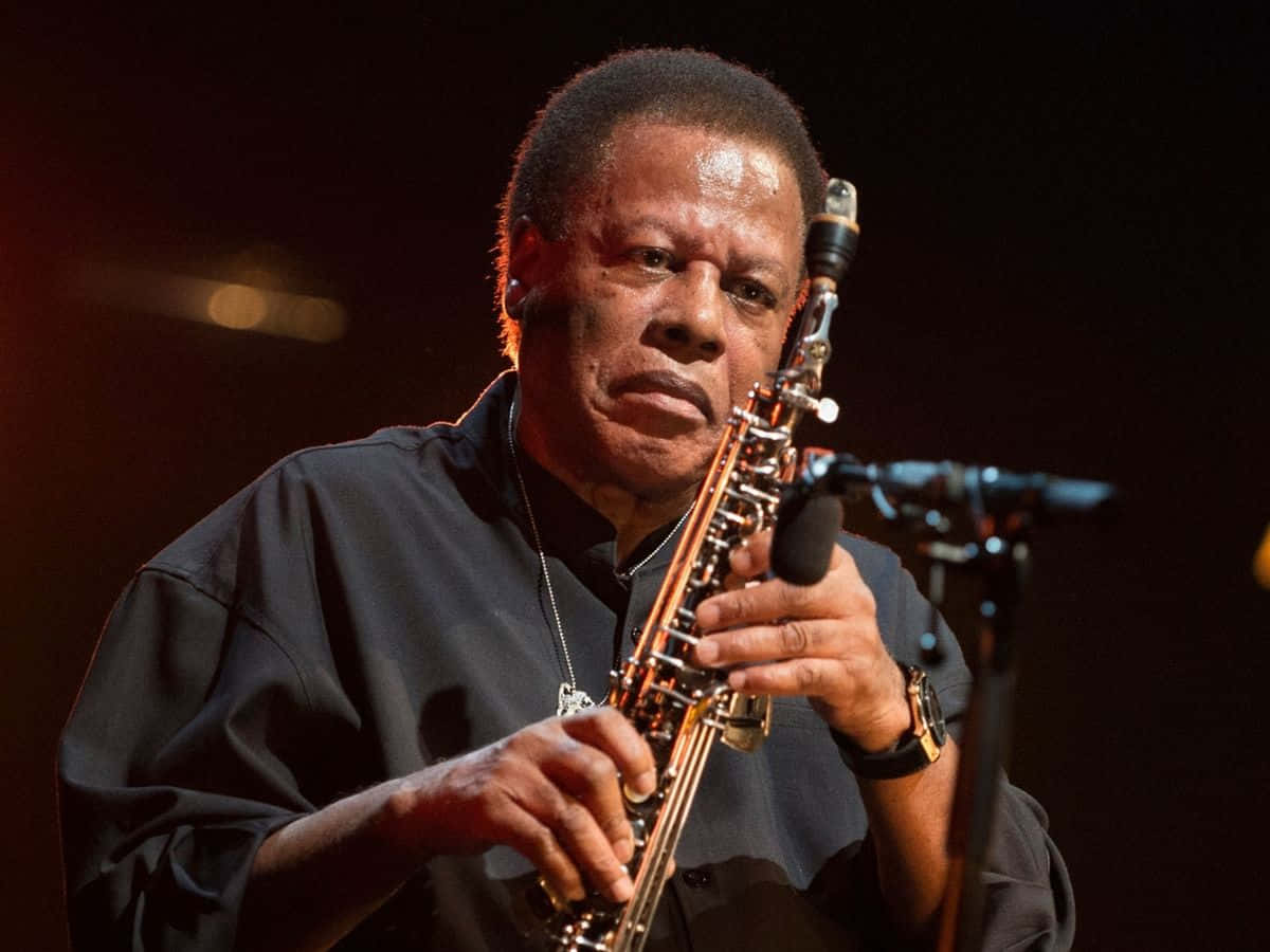 Wayne Shorter 桌布 壁紙 — 一位爵士音樂家在黑暗背景下於溫暖的舞台燈光下熱情地演奏色士風。
