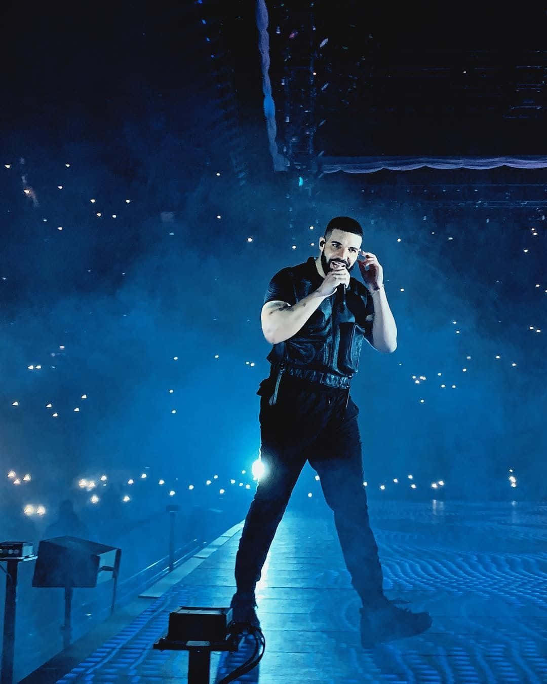 Drake 桌布 壁紙 — 一位男性表演者在藍色燈光的舞台上，被發光的燈光和煙霧包圍，對著麥克風唱歌。