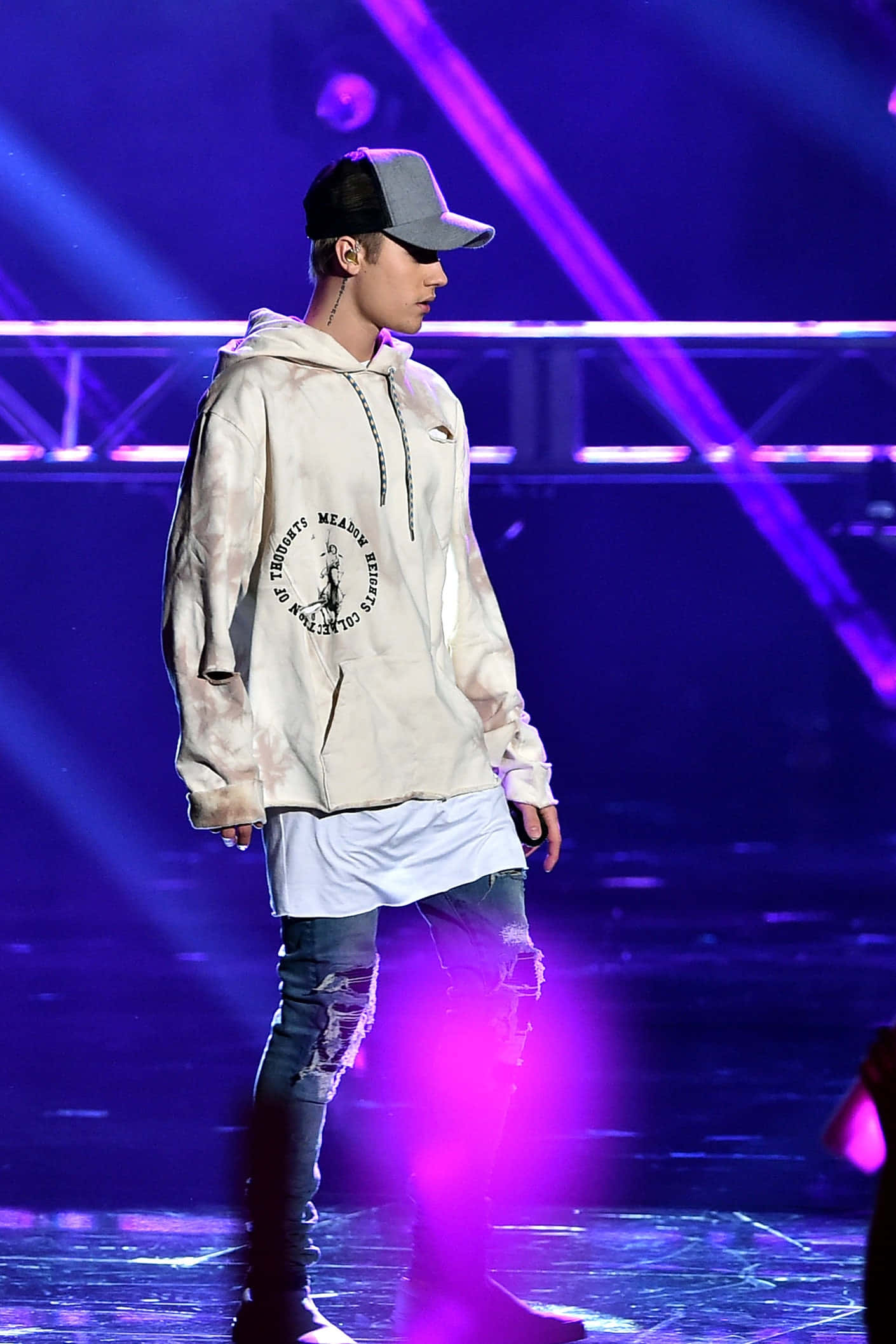 Justin Bieber 2015 壁紙 — 一位男性表演者穿著紮染連帽衫和破洞牛仔褲，站在充滿活力的紫色燈光舞台上，動態聚光燈下。