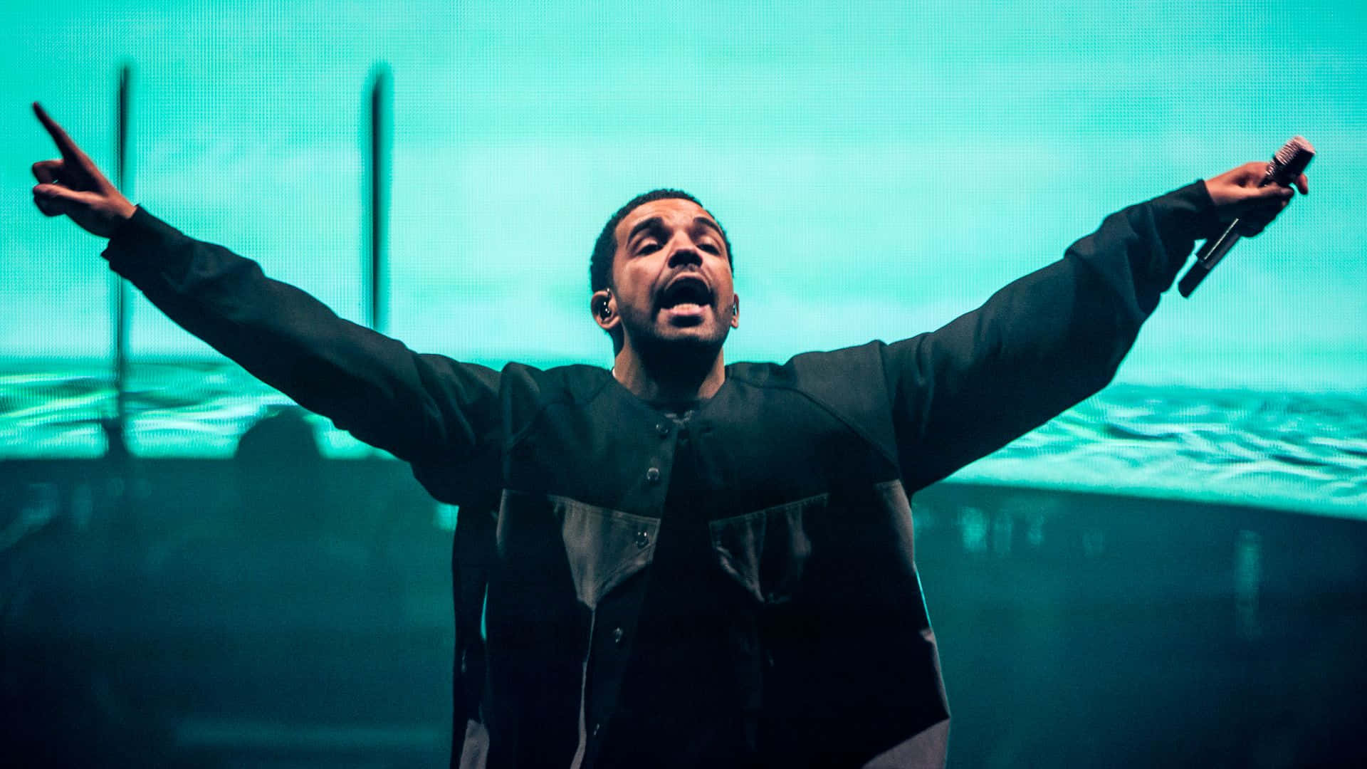 Drake 桌布 壁紙 — 一位男表演者張開雙臂，在充滿活力的青綠色燈光下熱情地唱歌。