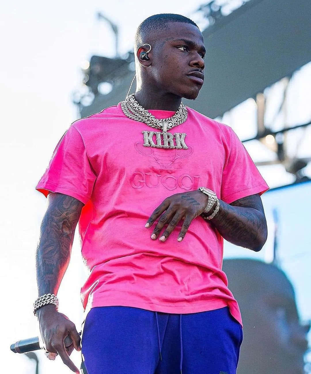 Dababy 桌布 壁紙 — 一位男饒舌歌手穿著亮粉紅色Gucci T恤和藍色褲子，帶著紋身和金鏈在舞台上表演。
