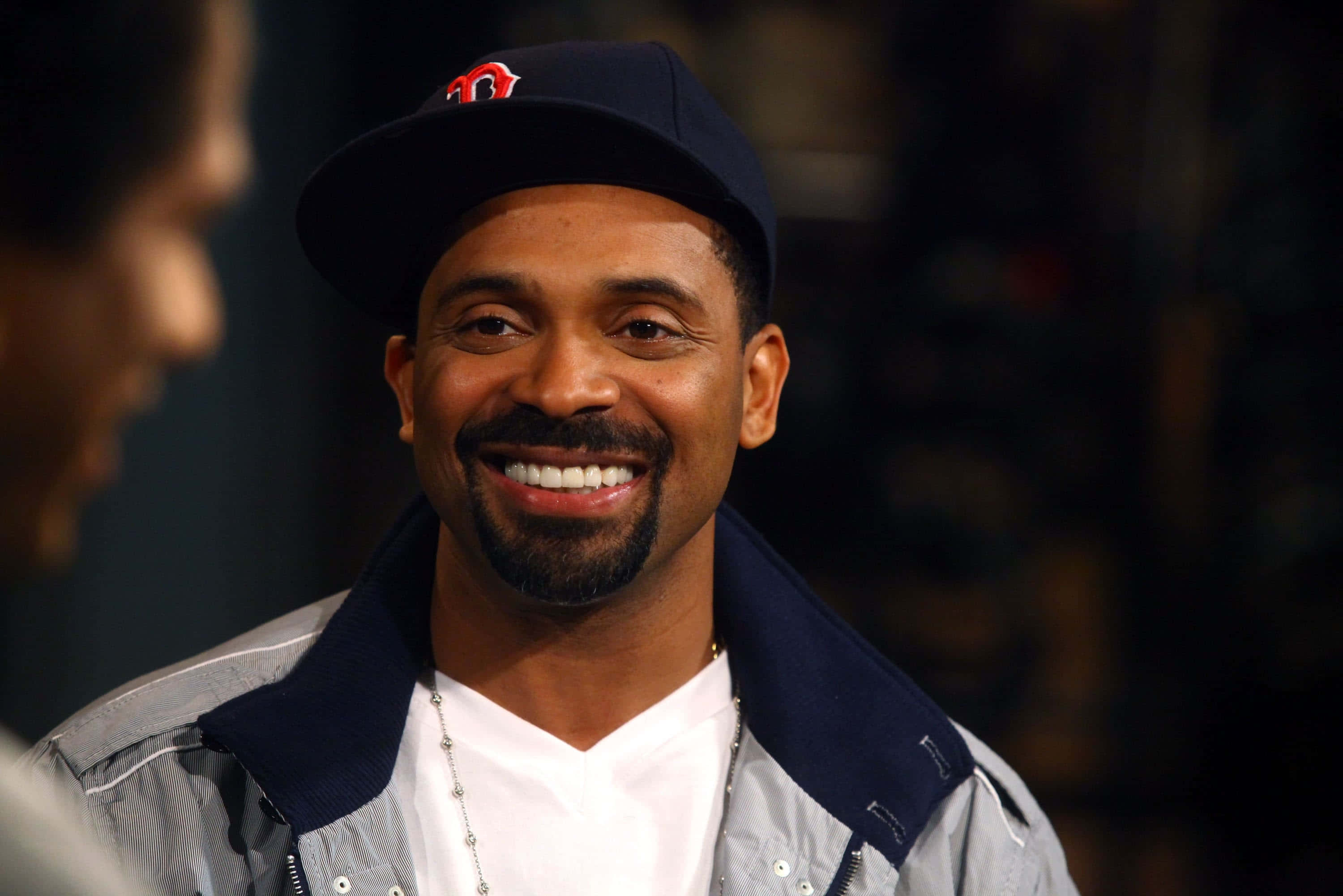 Mike Epps 桌布 壁紙 — 一位留著山羊鬍的微笑男士戴著海軍藍帽子和灰色外套，正在交談。