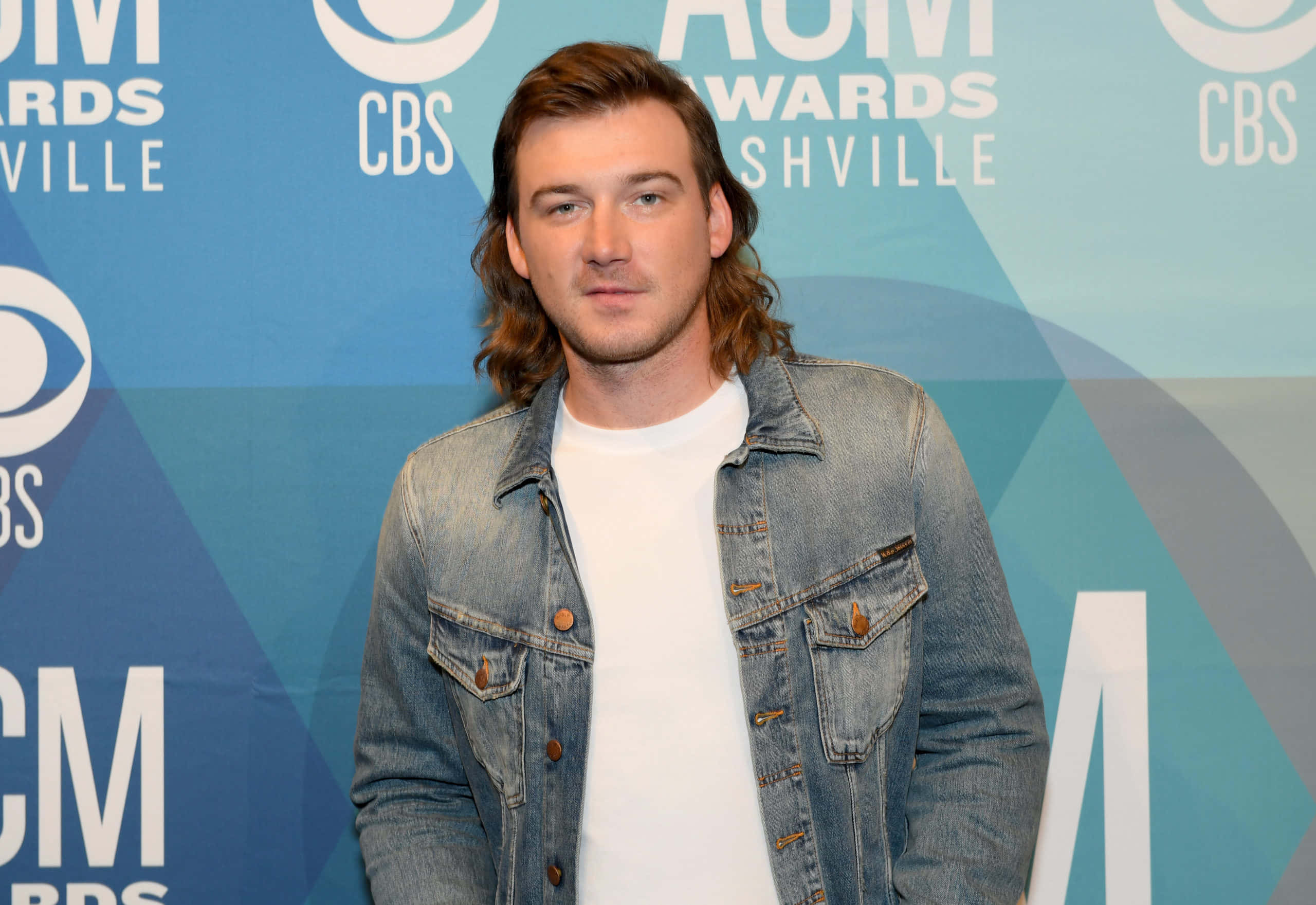 Morgan Wallen 桌布 壁紙 — 一位留著棕色長髮的男子在ACM頒獎禮納什維爾紅地毯上，身穿白色T恤外搭牛仔外套。