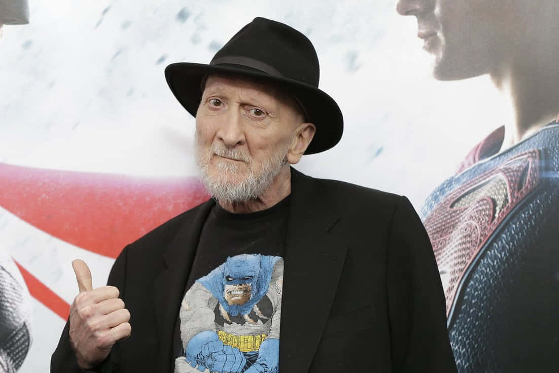 Frank Miller 桌布 壁紙 — 一位留著白鬍子、戴黑色紳士帽的長者，在超級英雄活動中穿著蝙蝠俠T恤豎起大拇指。