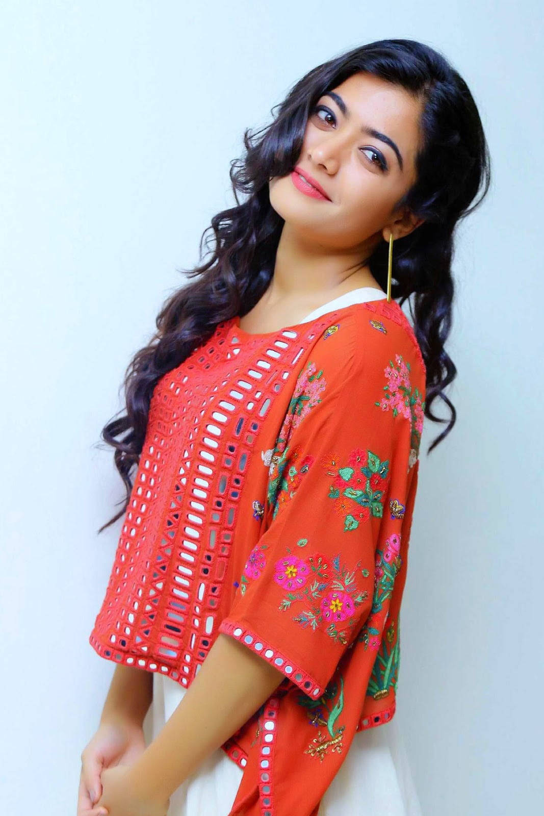 telugu 桌布 壁紙 — 一位留著長長深色捲髮的女性，身穿鮮紅色刺繡上衣，帶有花卉圖案和蕾絲鏤空設計，背景為純白色。