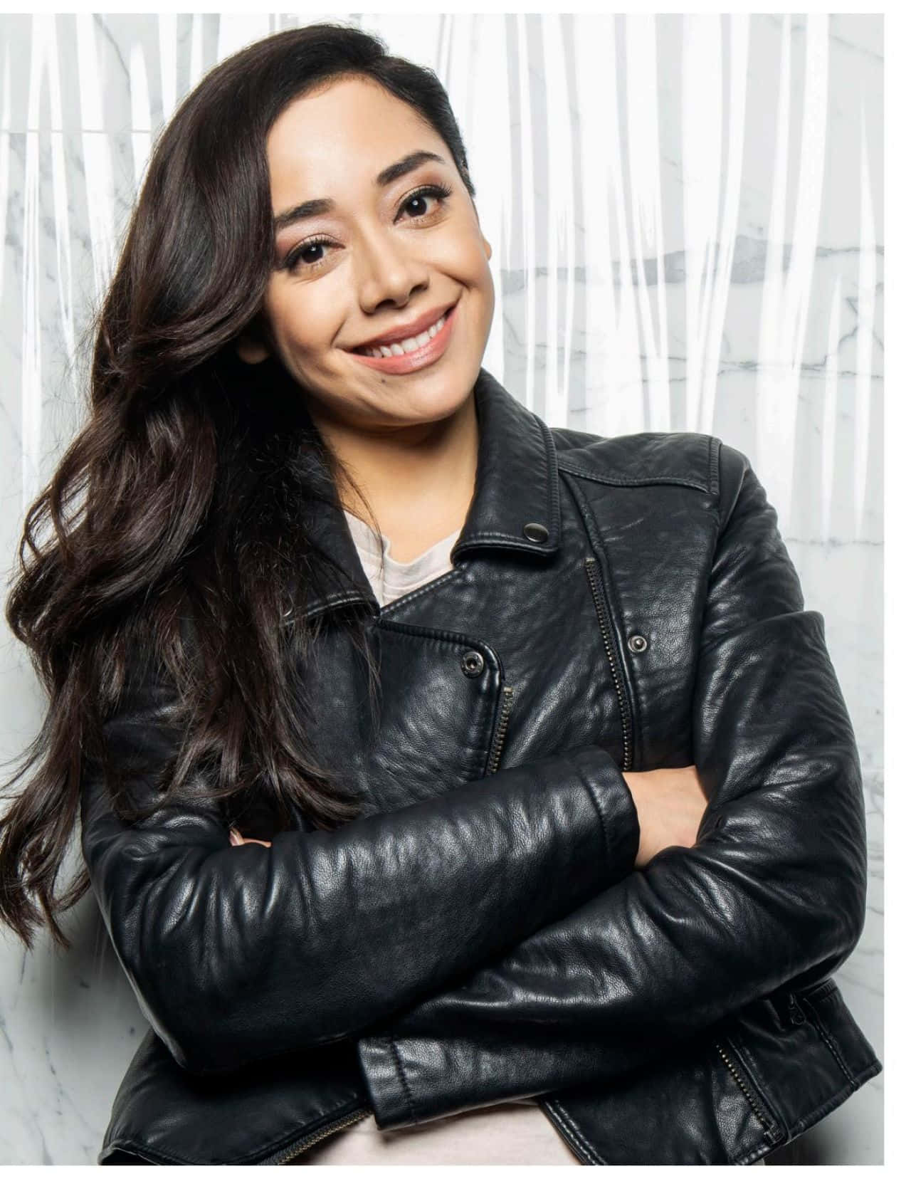 Aimee Garcia 桌布 壁紙 — 一位留著長黑髮的微笑女士，在白色大理石背景前穿著黑色皮褸。