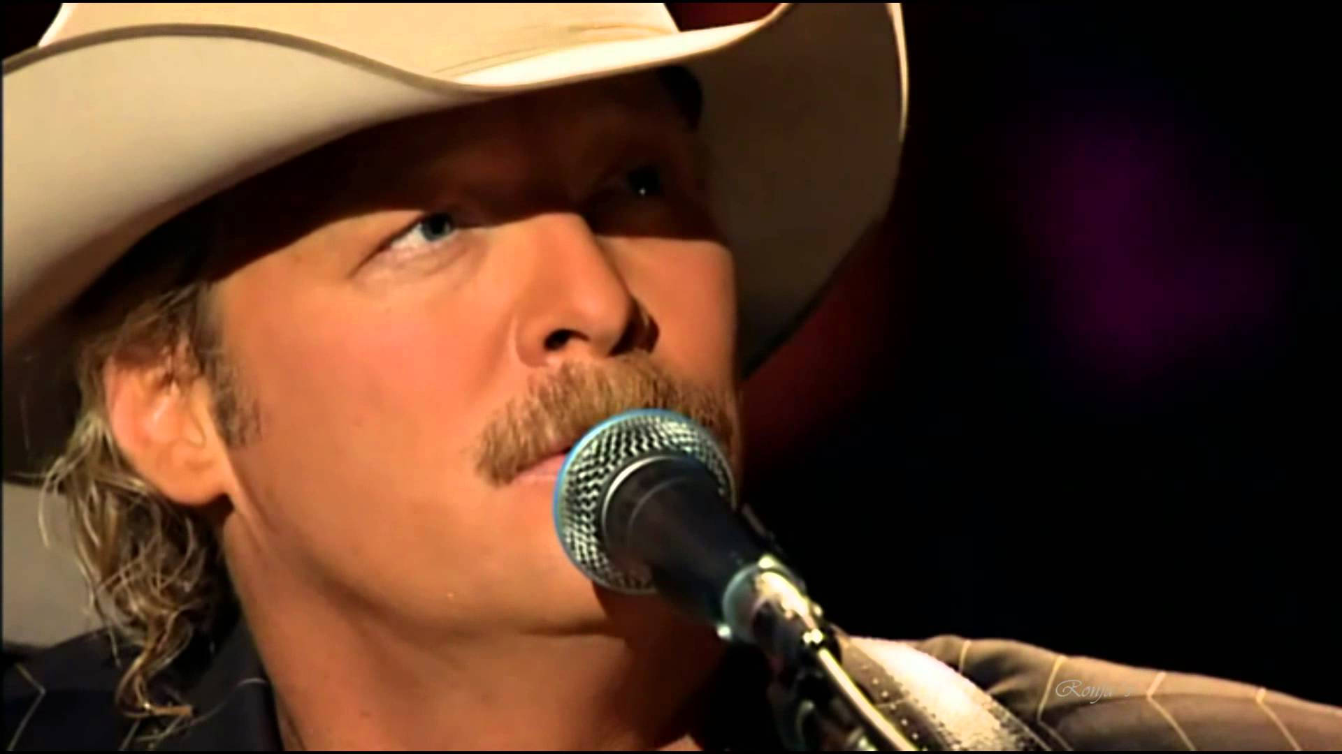 Alan Jackson 桌布 壁紙 — 一位留鬍子、戴白帽的牛仔歌手在舞台燈光下對著麥克風唱歌。