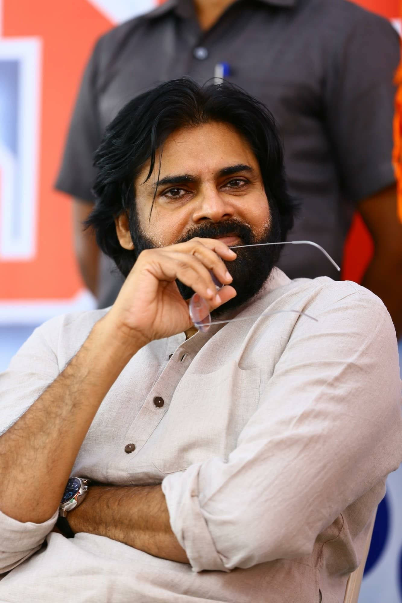 Pawan Kalyan 桌布 壁紙 — 一位留鬍子、深色頭髮的男子，穿著淺色襯衫，手持眼鏡對著鏡頭微笑。
