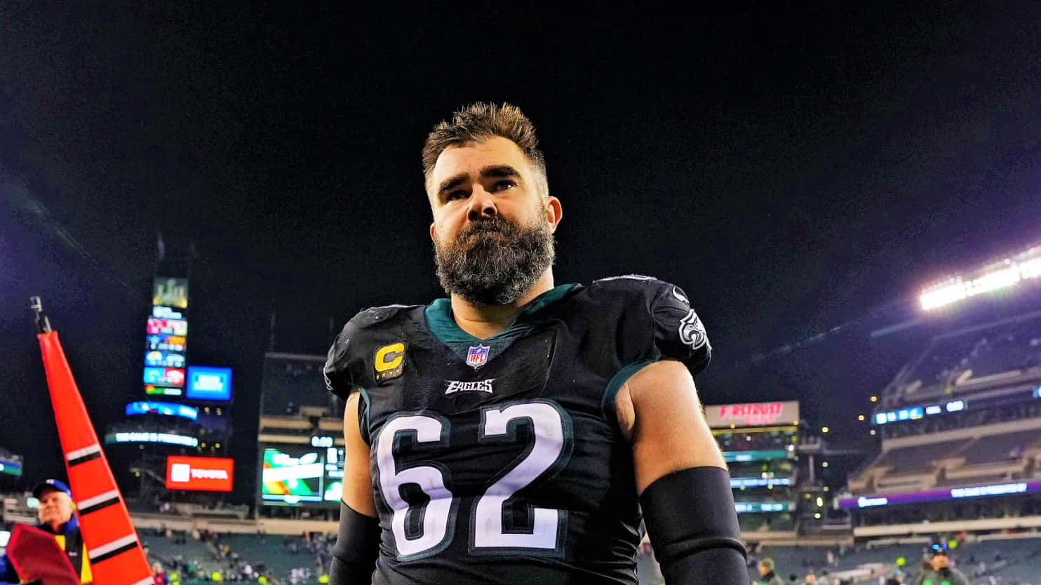 Jason Kelce 桌布 壁紙 — 一位留鬍子的NFL球員身穿黑色Eagles球衣，在夜晚燈光明亮的球場上莊嚴地站立。