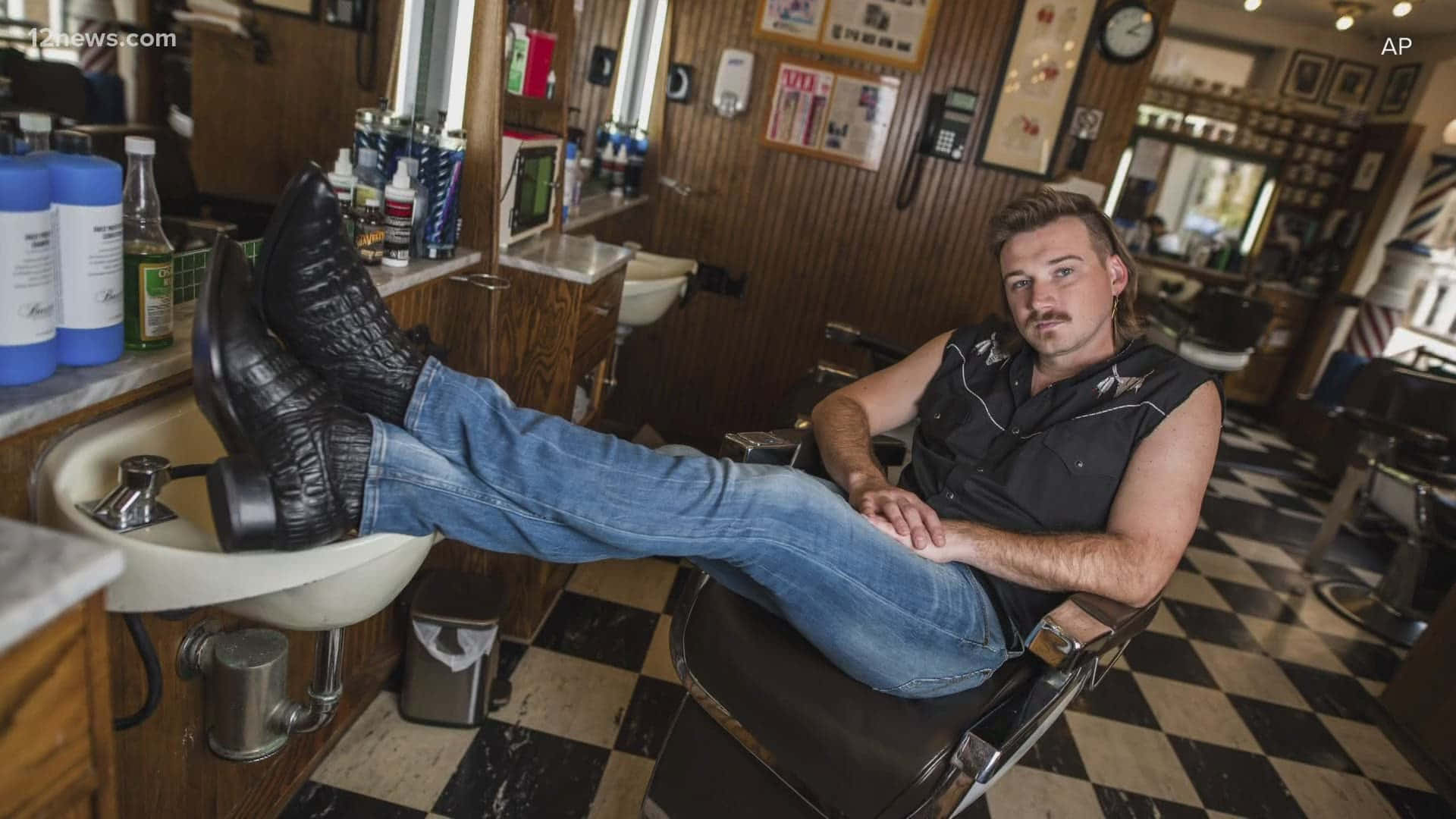 Morgan Wallen 桌布 壁紙 — 一位留鬍子的男人在復古理髮店裡，將靴子擱在水槽上，懶洋洋地躺在理髮椅上。