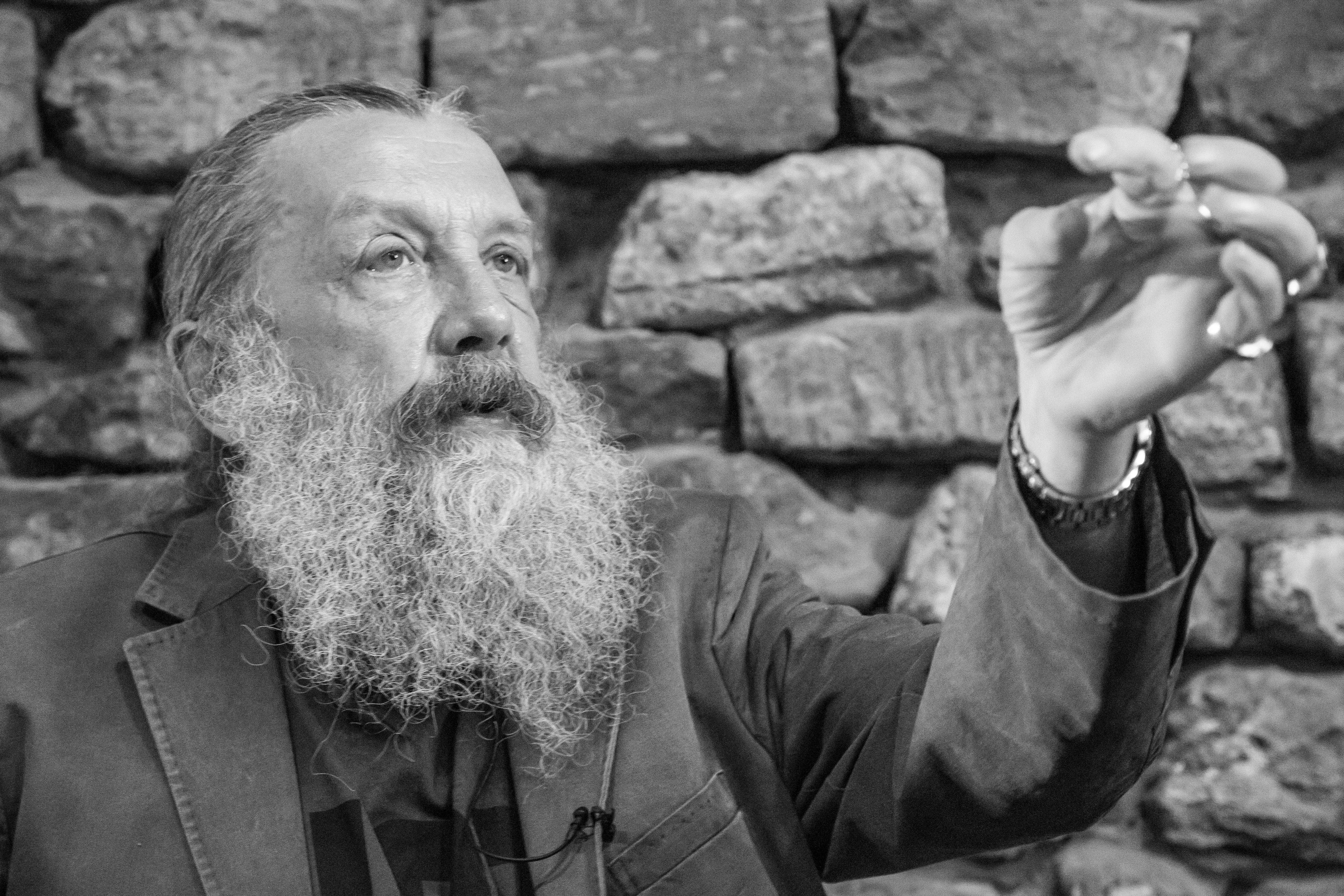 Alan Moore 桌布 壁紙 — 一位留鬍子的男士身穿西裝，在紋理石牆前若有所思地做手勢，是一張引人注目的黑白肖像照。