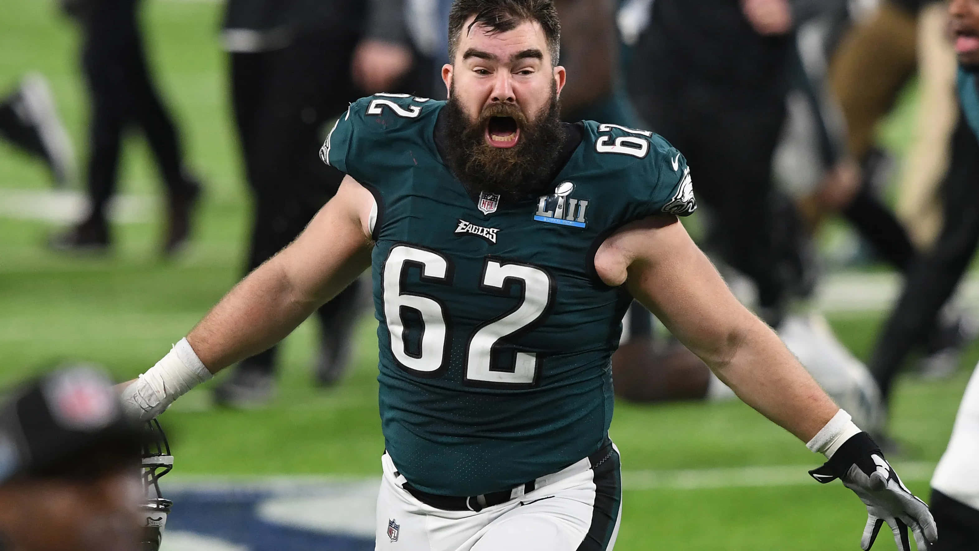 Jason Kelce 桌布 壁紙 — 一位留鬍子的費城老鷹隊美式足球員，身穿62號球衣，在球場上張開雙臂熱情慶祝。