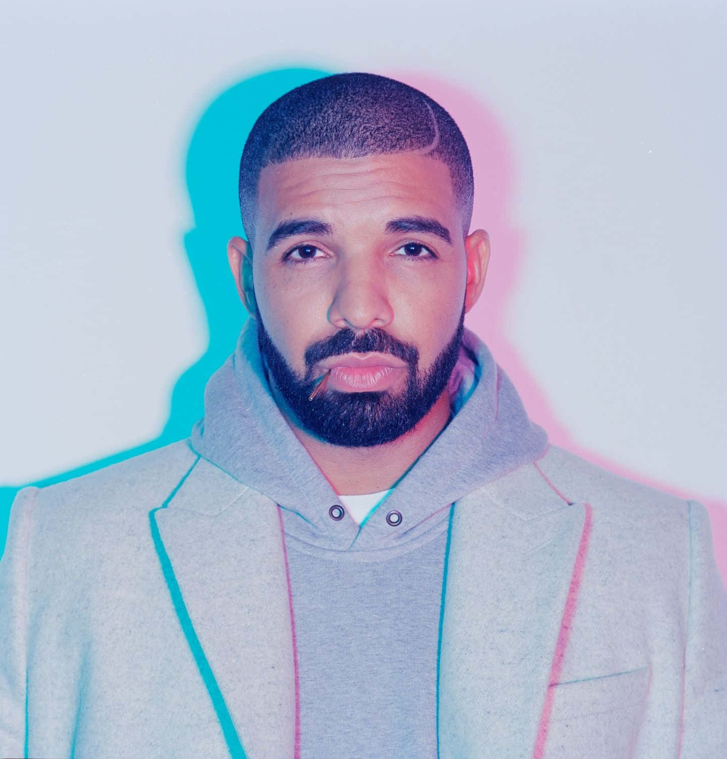 Drake 桌布 壁紙 — 一位留鬍子短髮的男子穿著灰色連帽衫，外搭西裝外套，青色和粉紅色的霓虹燈在他身後投射出色彩繽紛的影子。