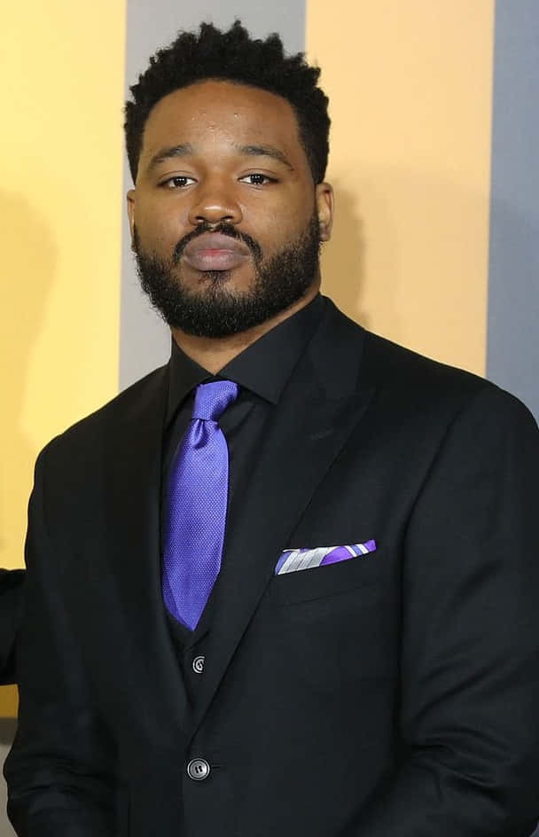 Ryan Coogler 桌布 壁紙 — 一位留鬍子短髮的男子穿著黑色西裝，配搭鮮紫色領帶，背景是黃色和灰色條紋。