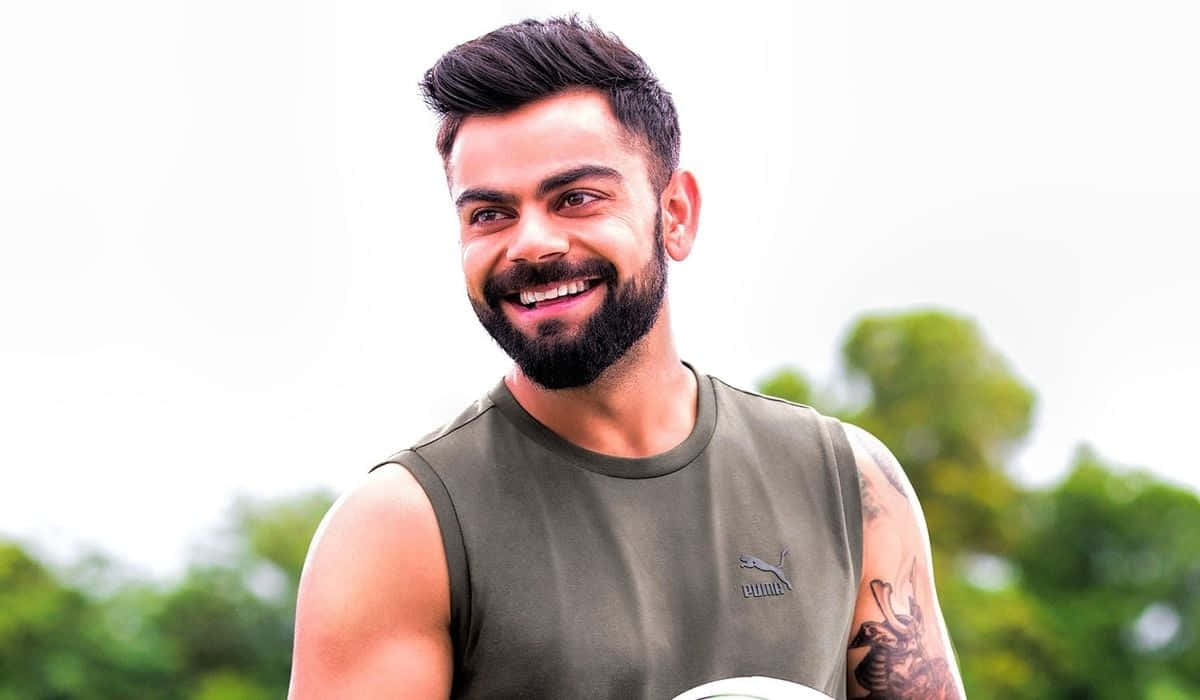 Virat Kohli 桌布 壁紙 — 一位留鬍鬚、手臂有紋身的微笑男子，在模糊的綠色背景下拿著板球。