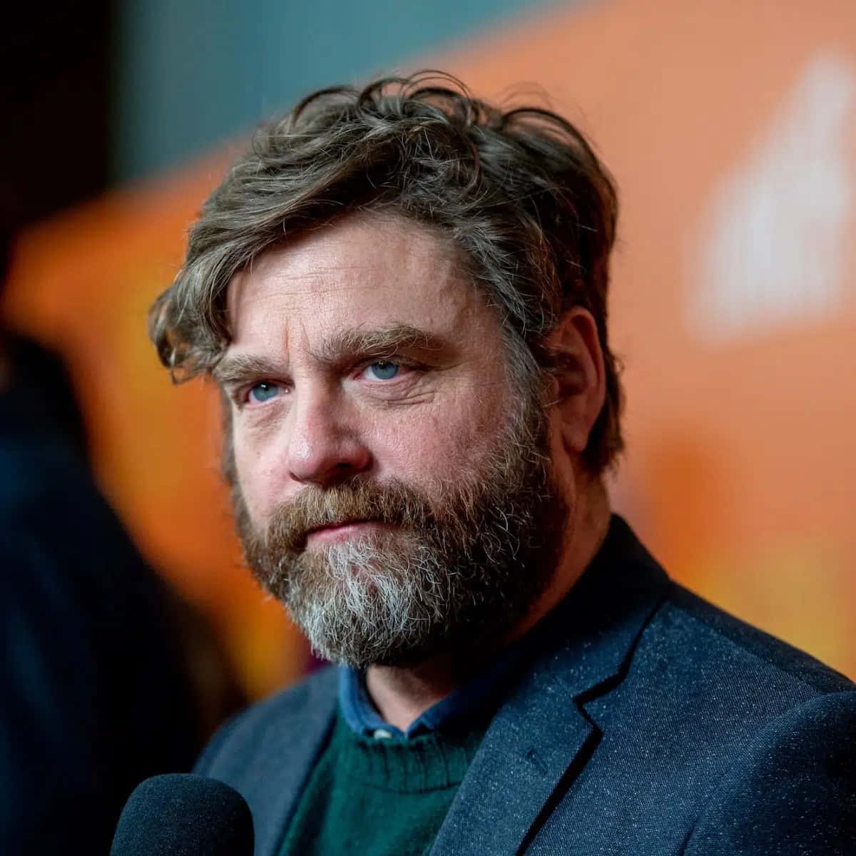 Zach Galifianakis 桌布 壁紙 — 一位留鬍鬚、擁有強烈藍色眼睛的男子直視鏡頭，對著麥克風說話的特寫照片。