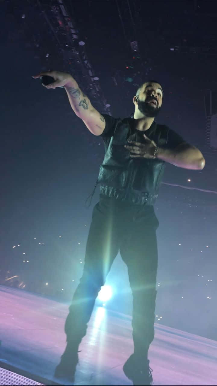 Drake 桌布 壁紙 — 一位留鬍鬚、有紋身的男士在昏暗的舞台上，在明亮的聚光燈和煙霧效果下表演。