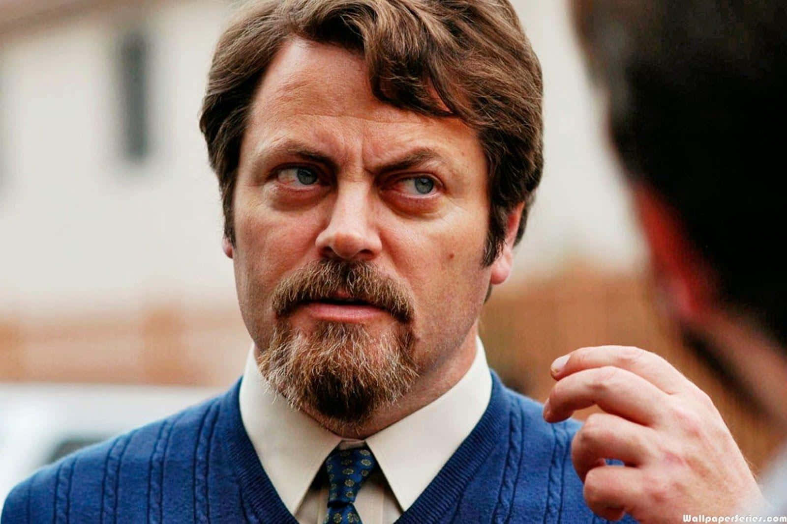 nick offerman 桌布 壁紙 — 一位留鬍鬚、藍眼睛的男人穿著藍色毛衣和領帶，專注地看著鏡頭外的某人。