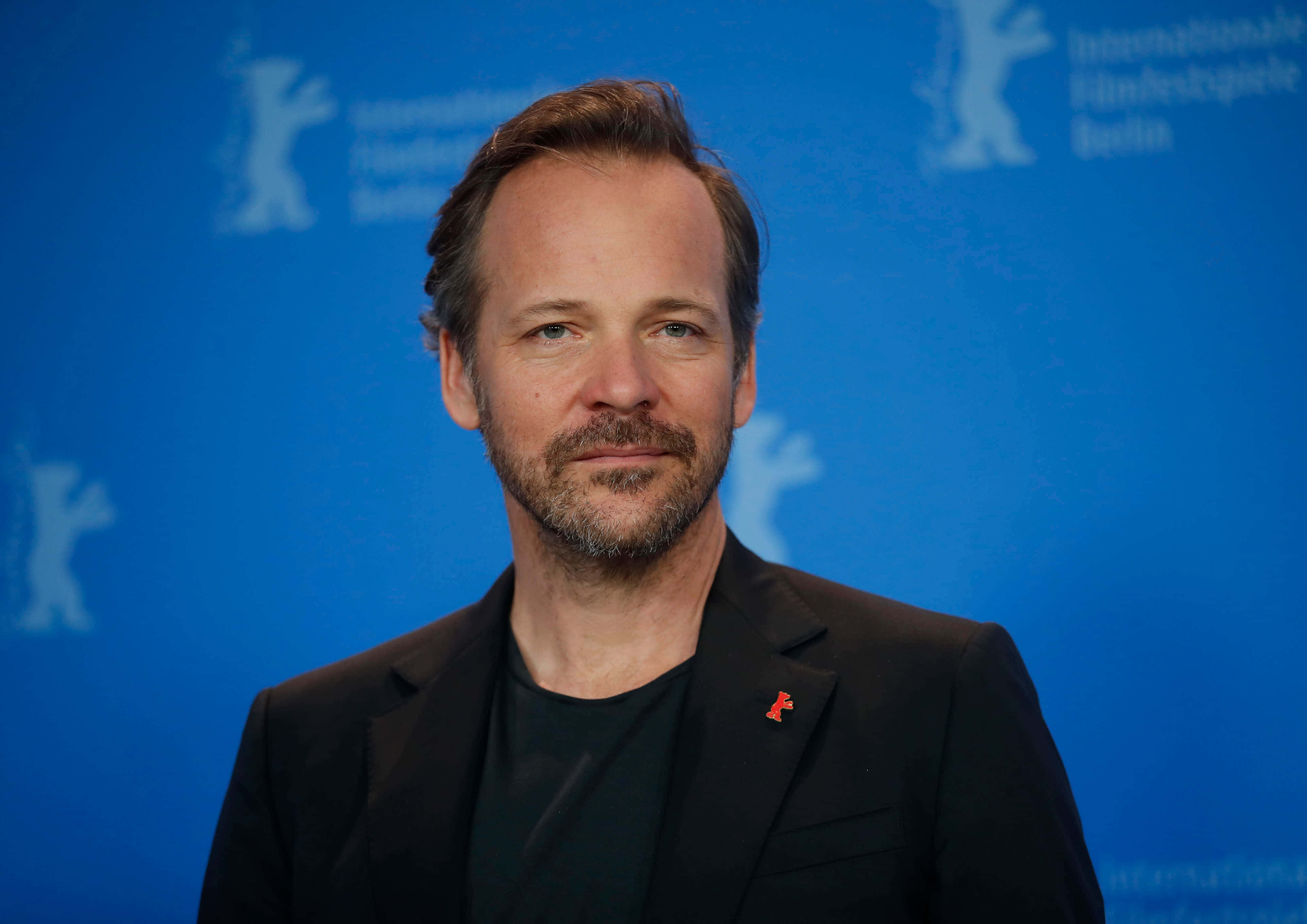 Peter Sarsgaard 桌布 壁紙 — 一位留鬍鬚、身穿深色西裝的男子自信地站在柏林國際電影節的藍色背景前。