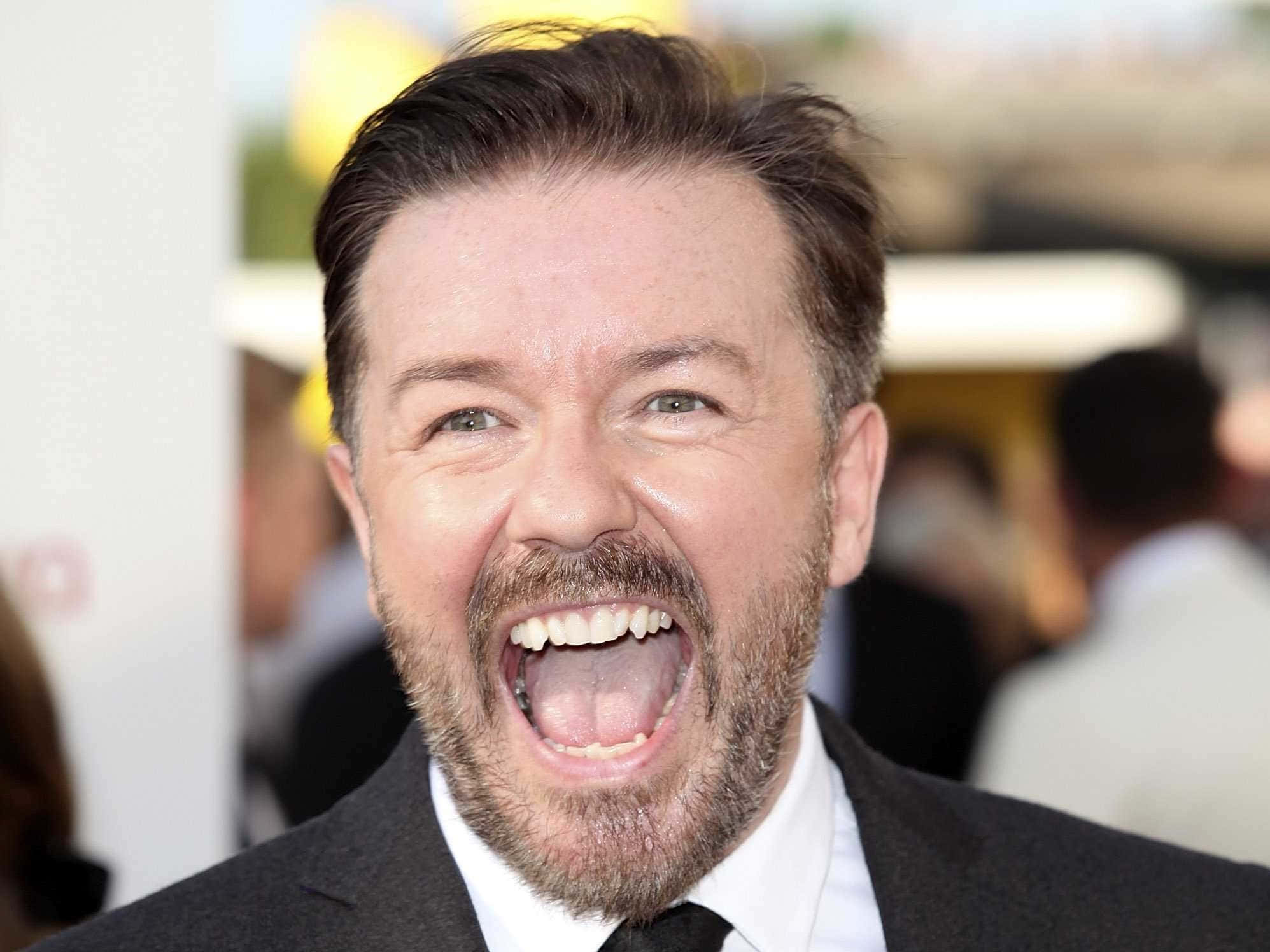 ricky gervais 桌布 壁紙 — 一位留鬍鬚、身穿西裝的男子在公開活動中張大嘴巴開懷大笑。