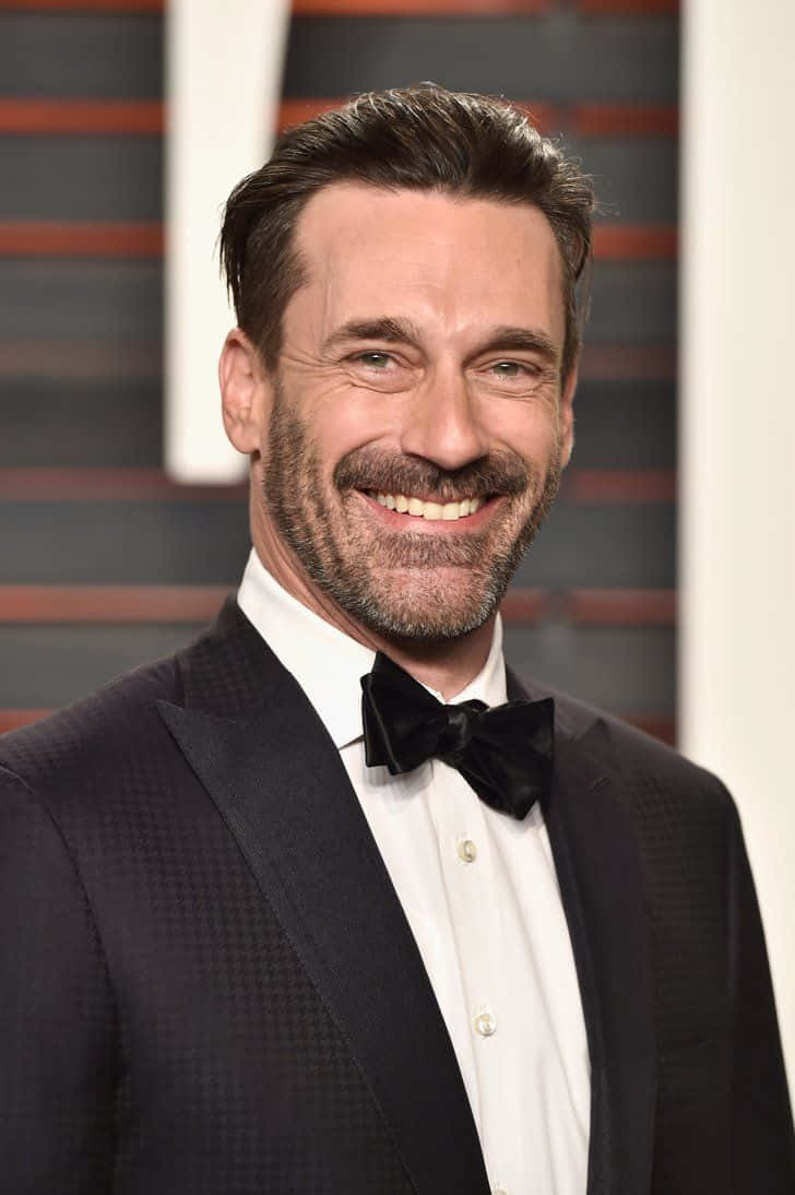 Jon Hamm 桌布 壁紙 — 一位留鬍鬚的微笑男士穿著黑色禮服和領結，背景為條紋圖案。