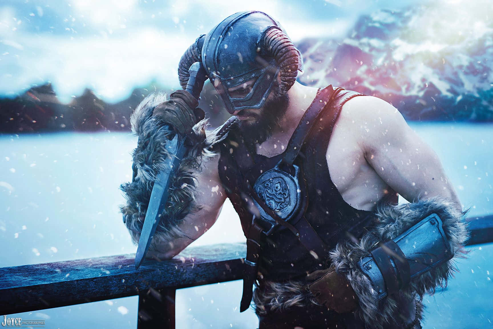dovahkiin 桌布 壁紙 — 一位留鬍鬚的戰士戴著角盔，倚靠在欄杆上，手持劍，雪花在群山背景下飄落。